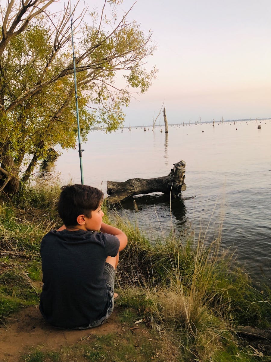 Young boy sitting watching the pink purple sunset of Lake Mulwala