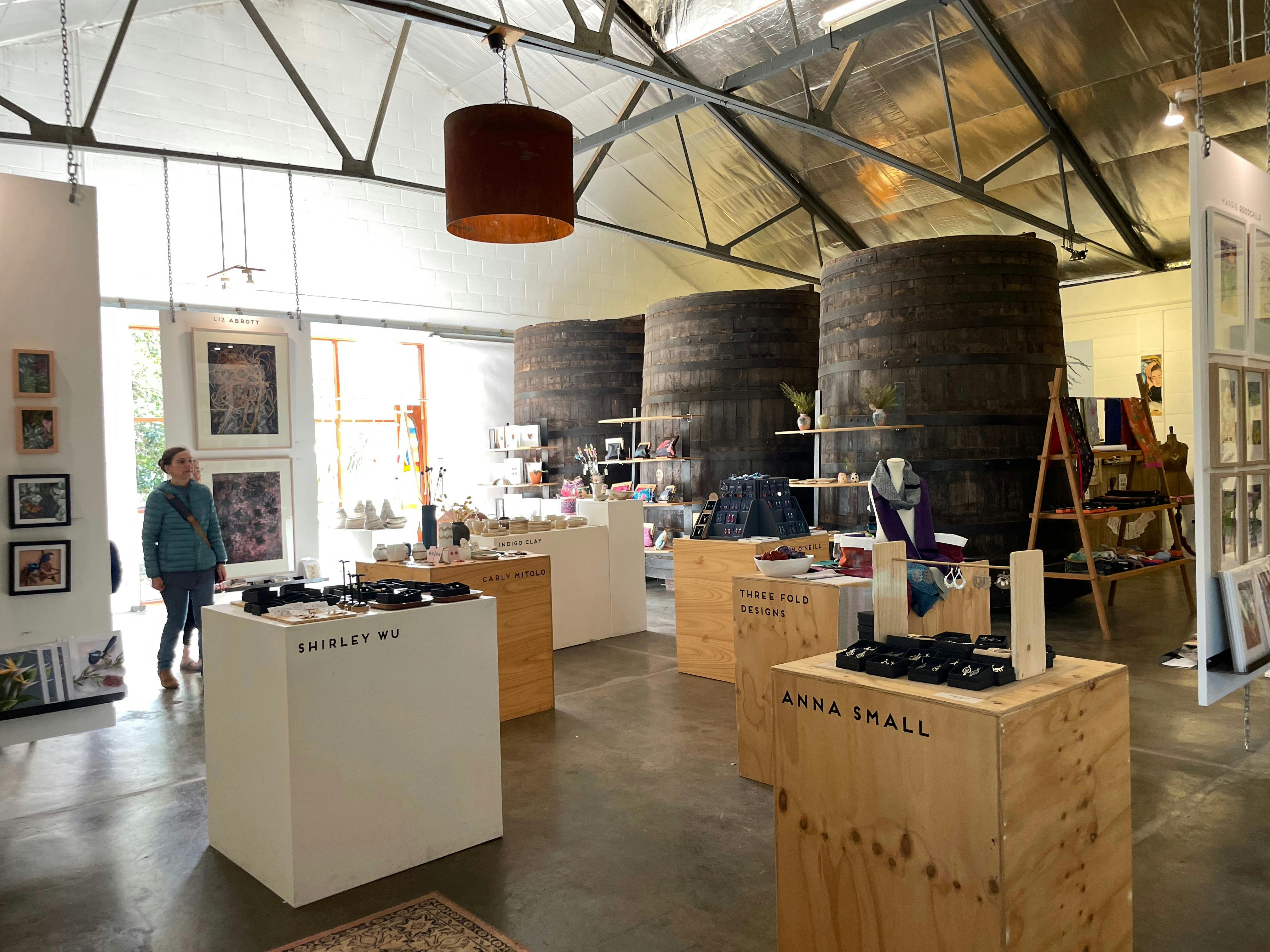 A room with art works on plinths with 3 giant barrels in the background
