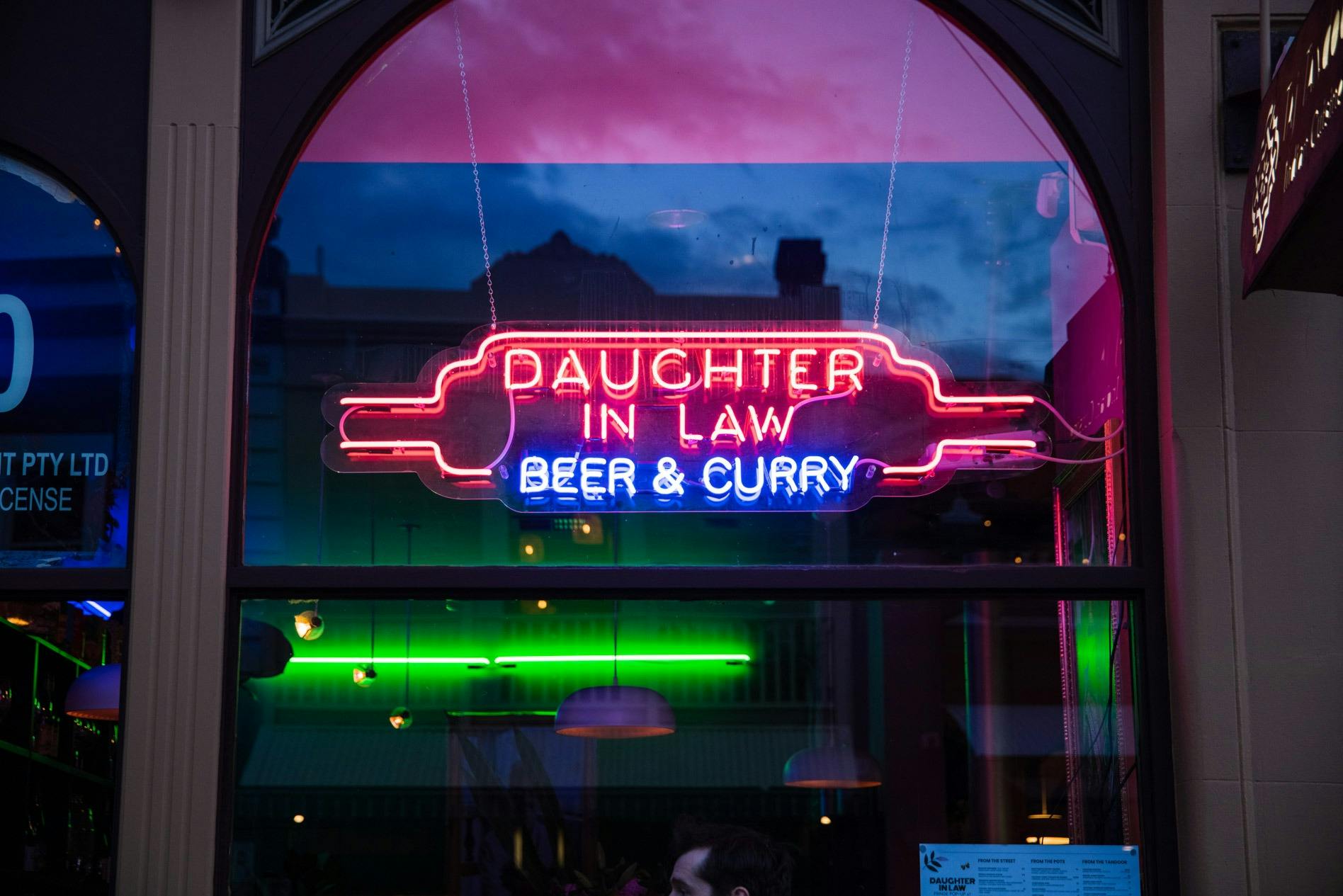 A pink neon sign saying 'Daughter in Law', with 'Beer & Curry' in blue below