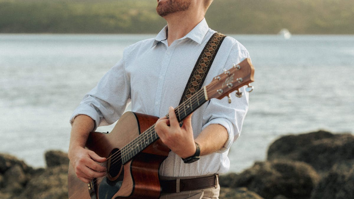 Image of a male musician playing a guitar standing on rocks on Hamilton Island