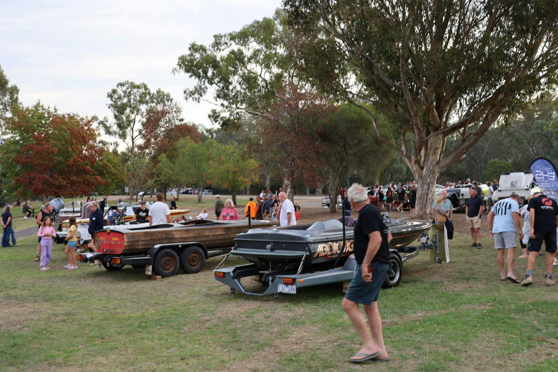 boats in a row on an open ground with people around them and trees