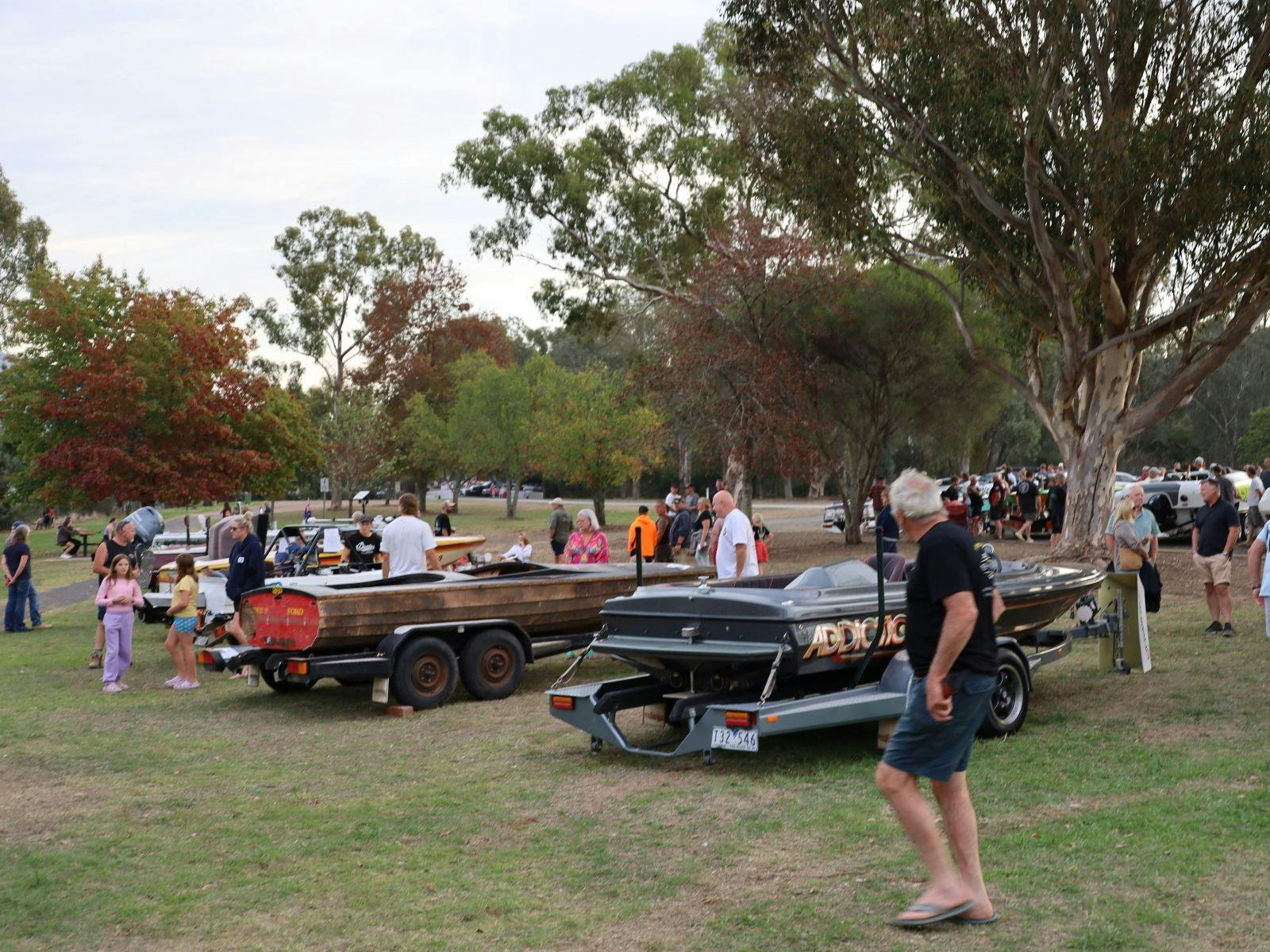 boats in a row on an open ground with people around them and trees