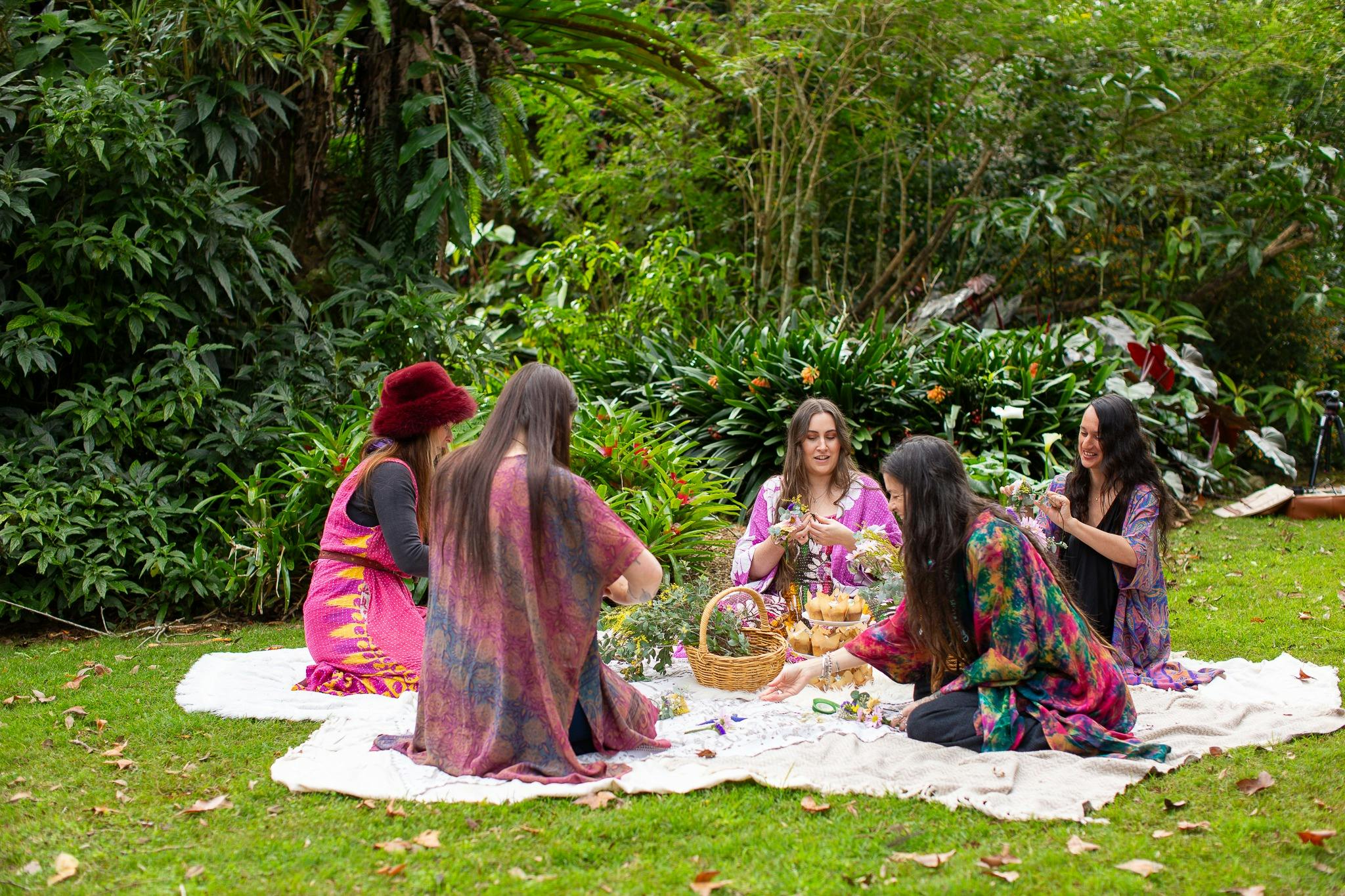 group of women sitting in a circle making flower crowns wearing colourful clothes