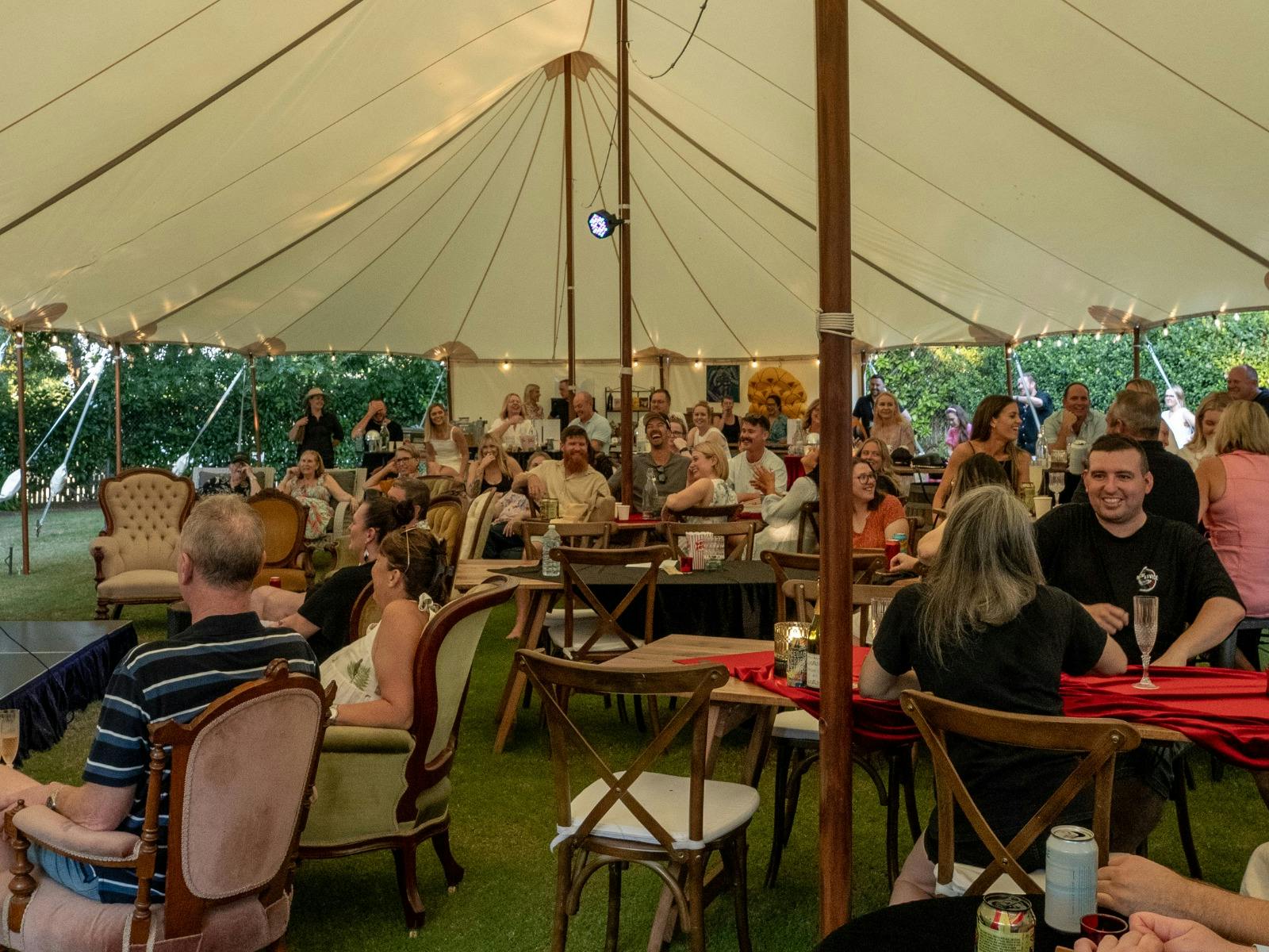 crowd of people sitting in ornate wooden furniture under a hamptons marquee