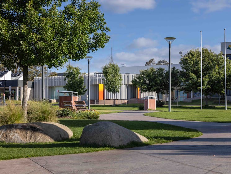 A path through a park leads to a contemporary building with bright segments.