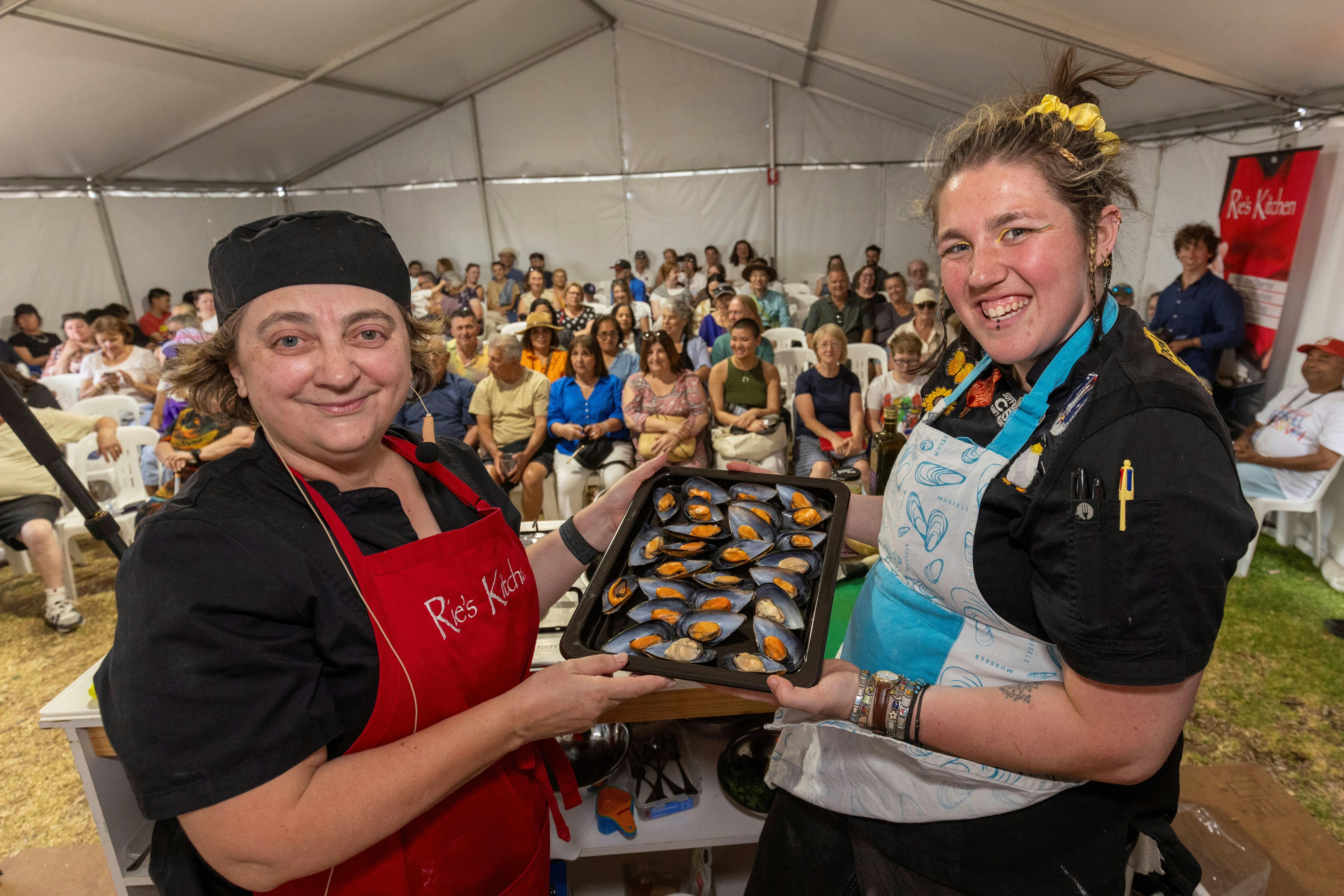 2 chefs in front of a crowd showing a tray of mussels