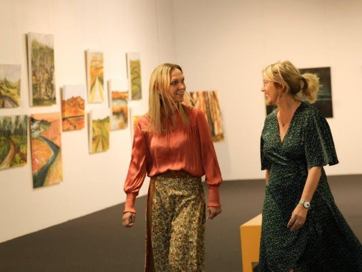 Two blonde women are animatedly speaking to each other as they walk through the Nulla Nulla Gallery