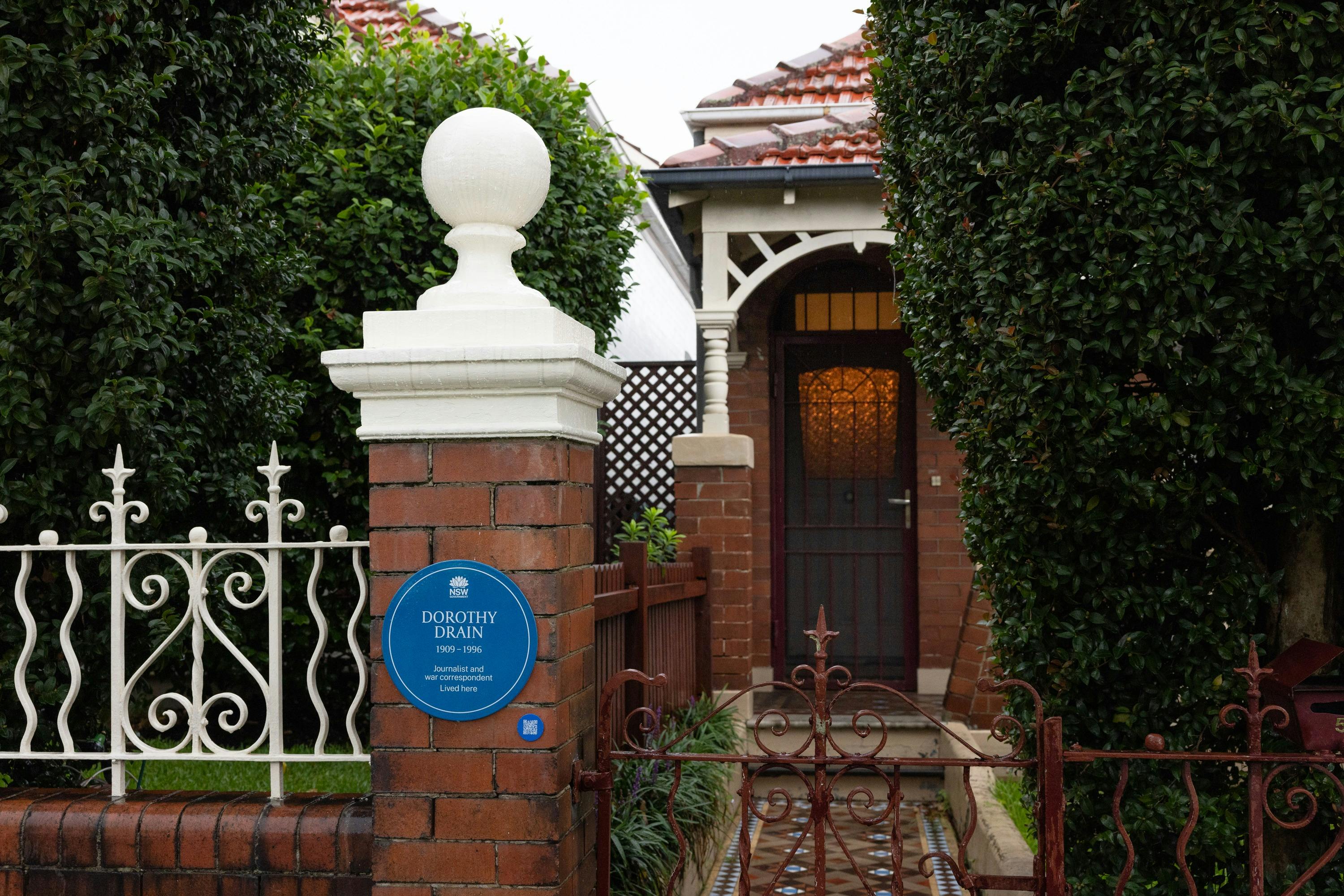 Blue plaque on brick fence post next to walkway to front door