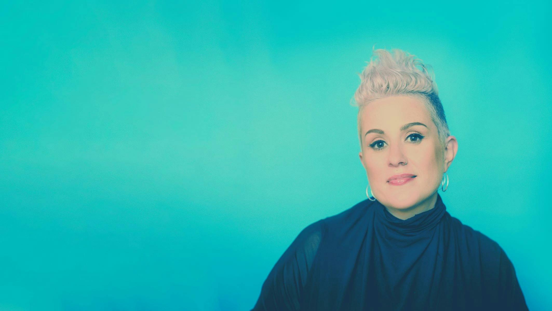 A person with short blonde hair stands against a vibrant blue background
