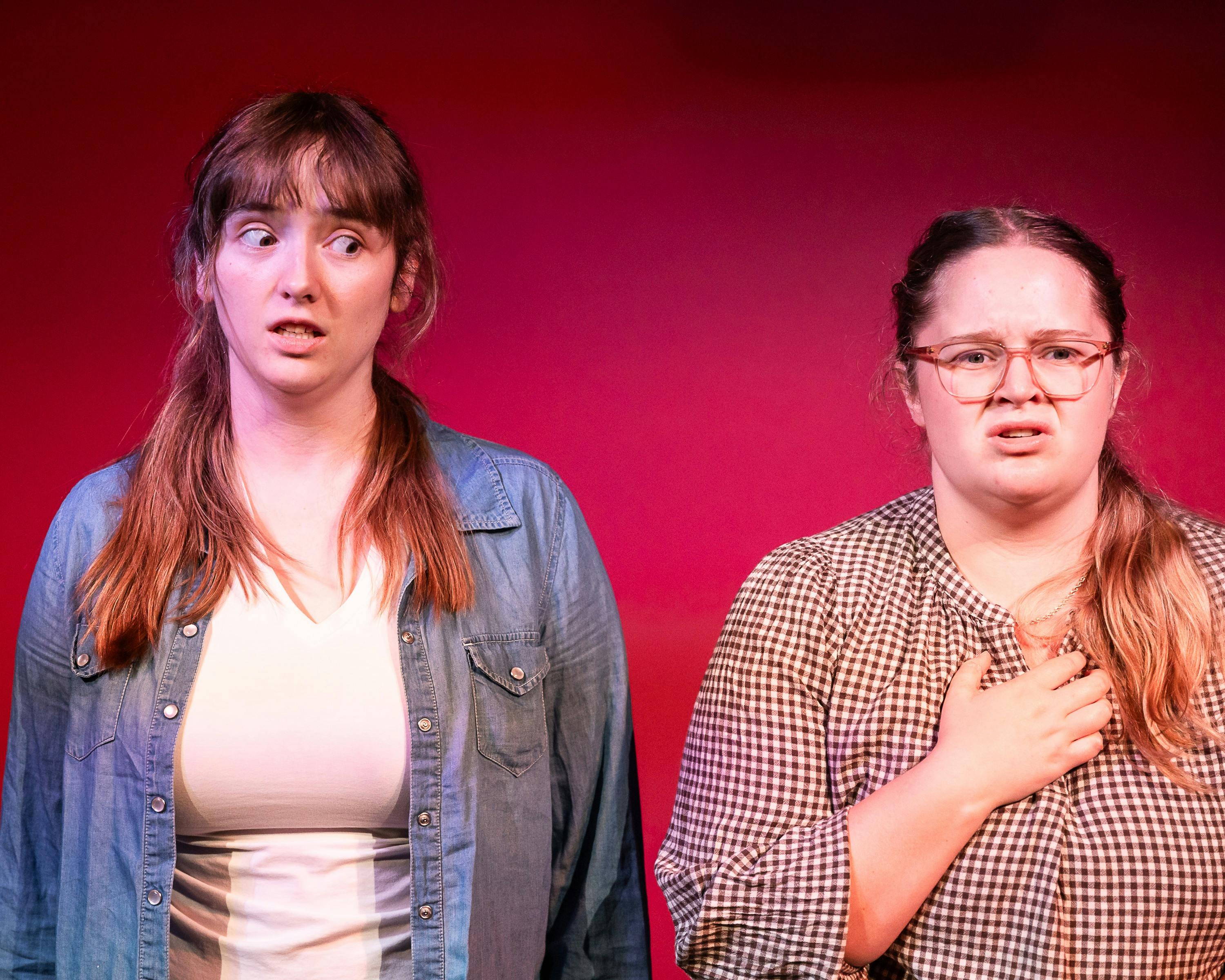 Two young women on stage stand side by side with anxious expressions.