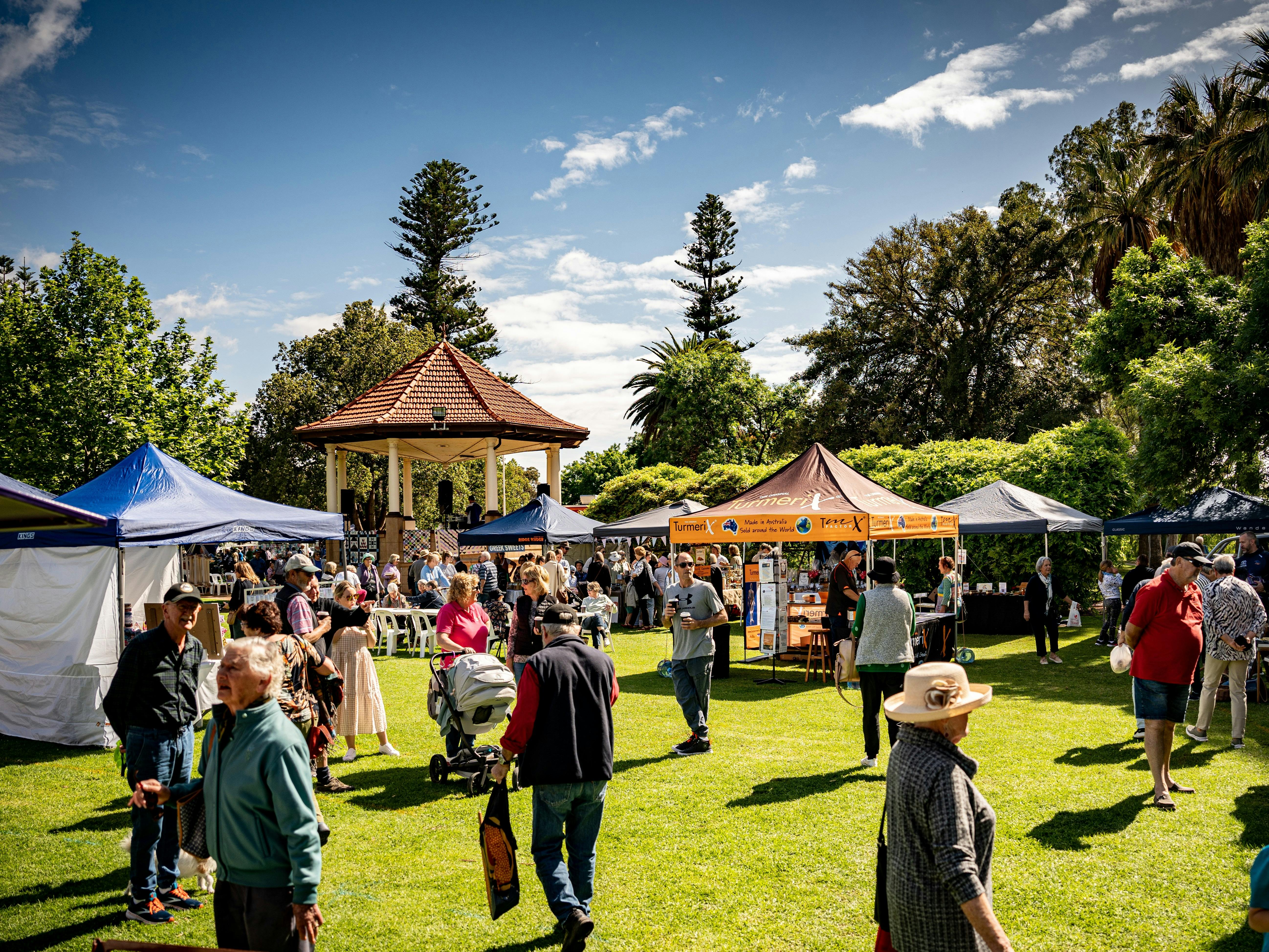 Visitors walk between outdoor market stalls displaying local products, crafts and handmade goods ben