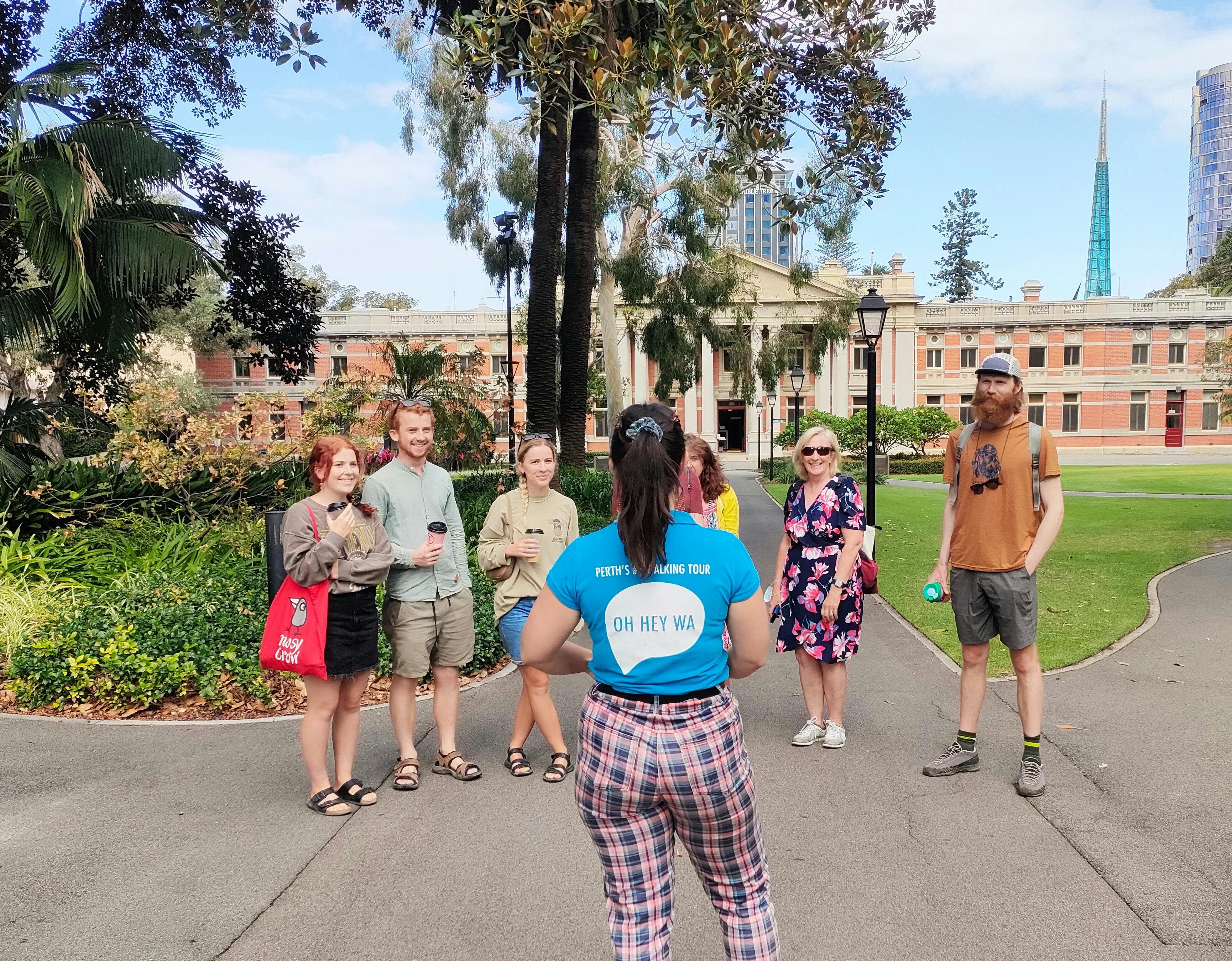 a tour guide presenting to a group of guests in a garden with a heritage building behind them