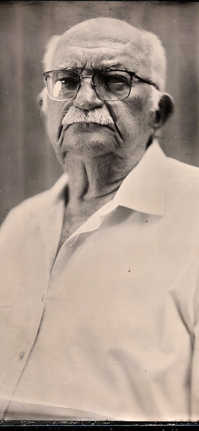 A black and white image of a man with a mustache and glasses with a stern look