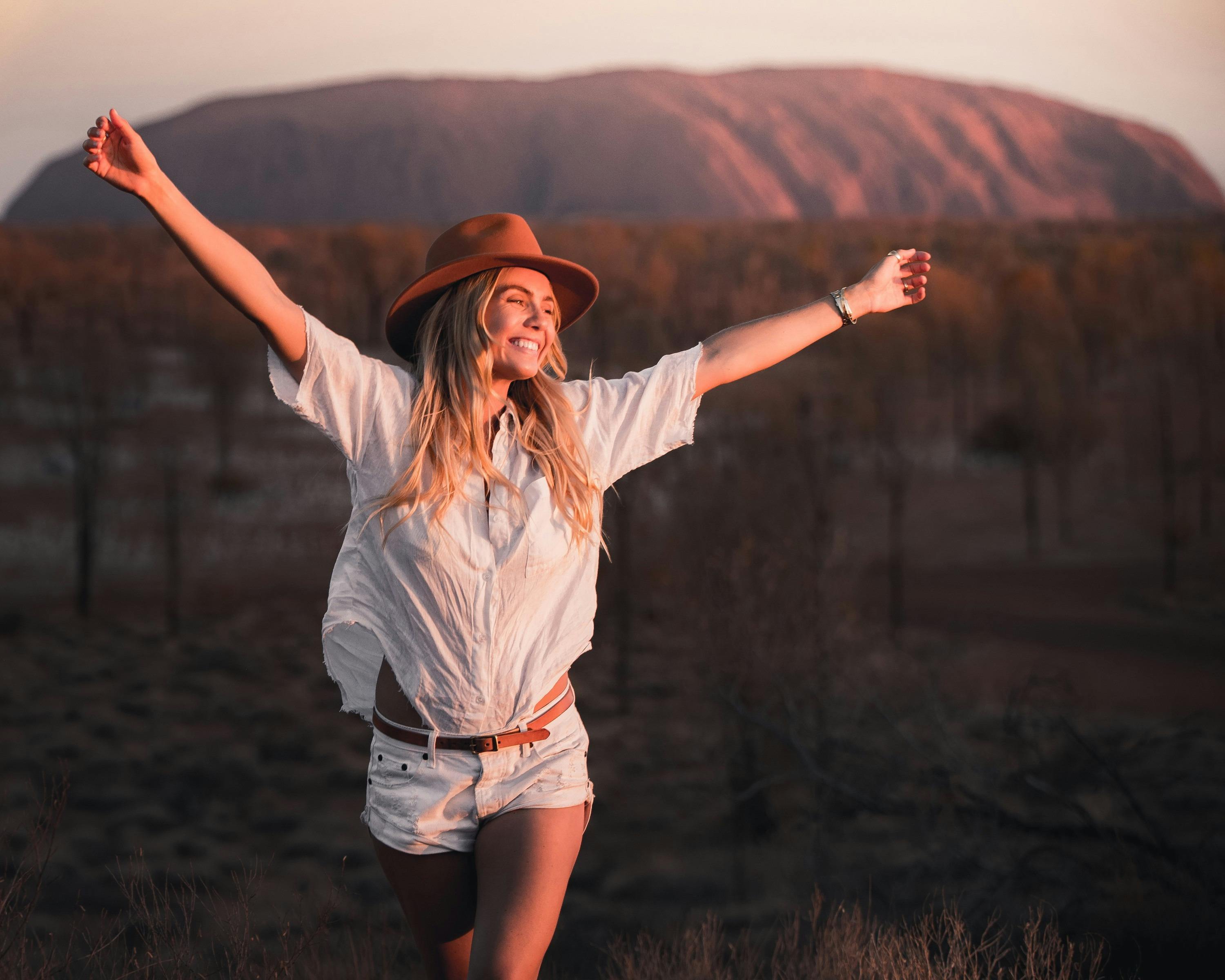 Girl stretching arms in the air smiling at the sunset in Uluru