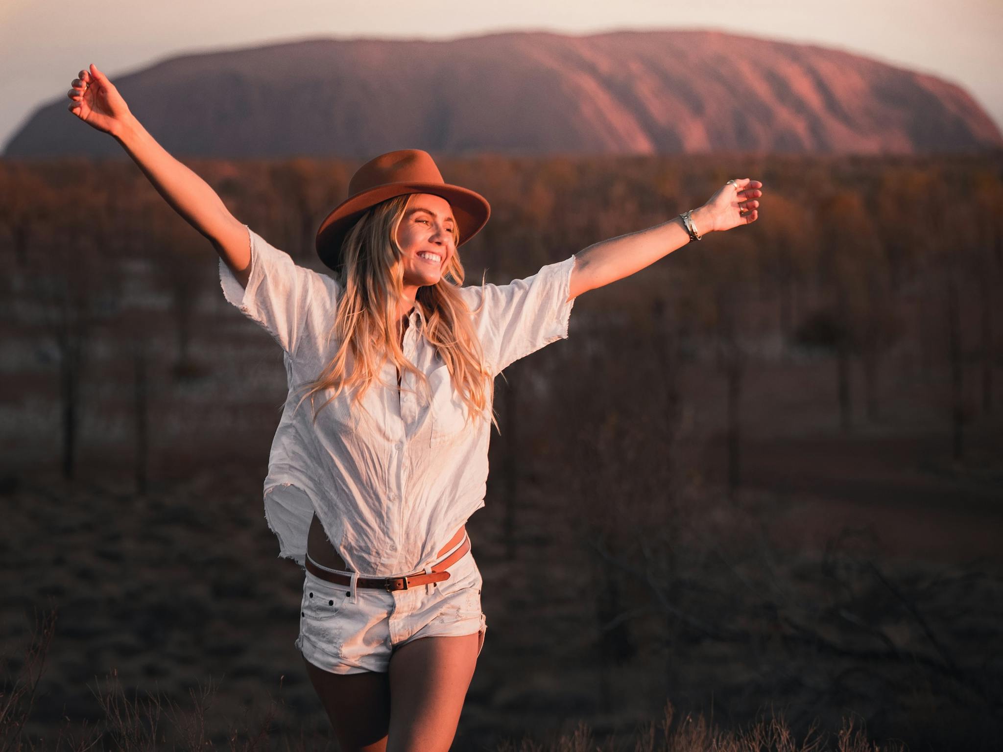 Girl stretching arms in the air smiling at the sunset in Uluru