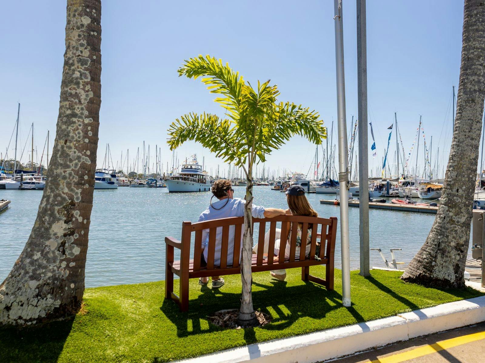 Man and Woman sitting on outdoor bench on the waterfront under palm trees Man and Woman sitting on outdoor bench on the waterfront under palm trees