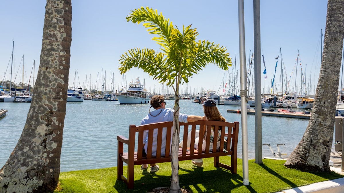 Man and Woman sitting on outdoor bench on the waterfront under palm trees