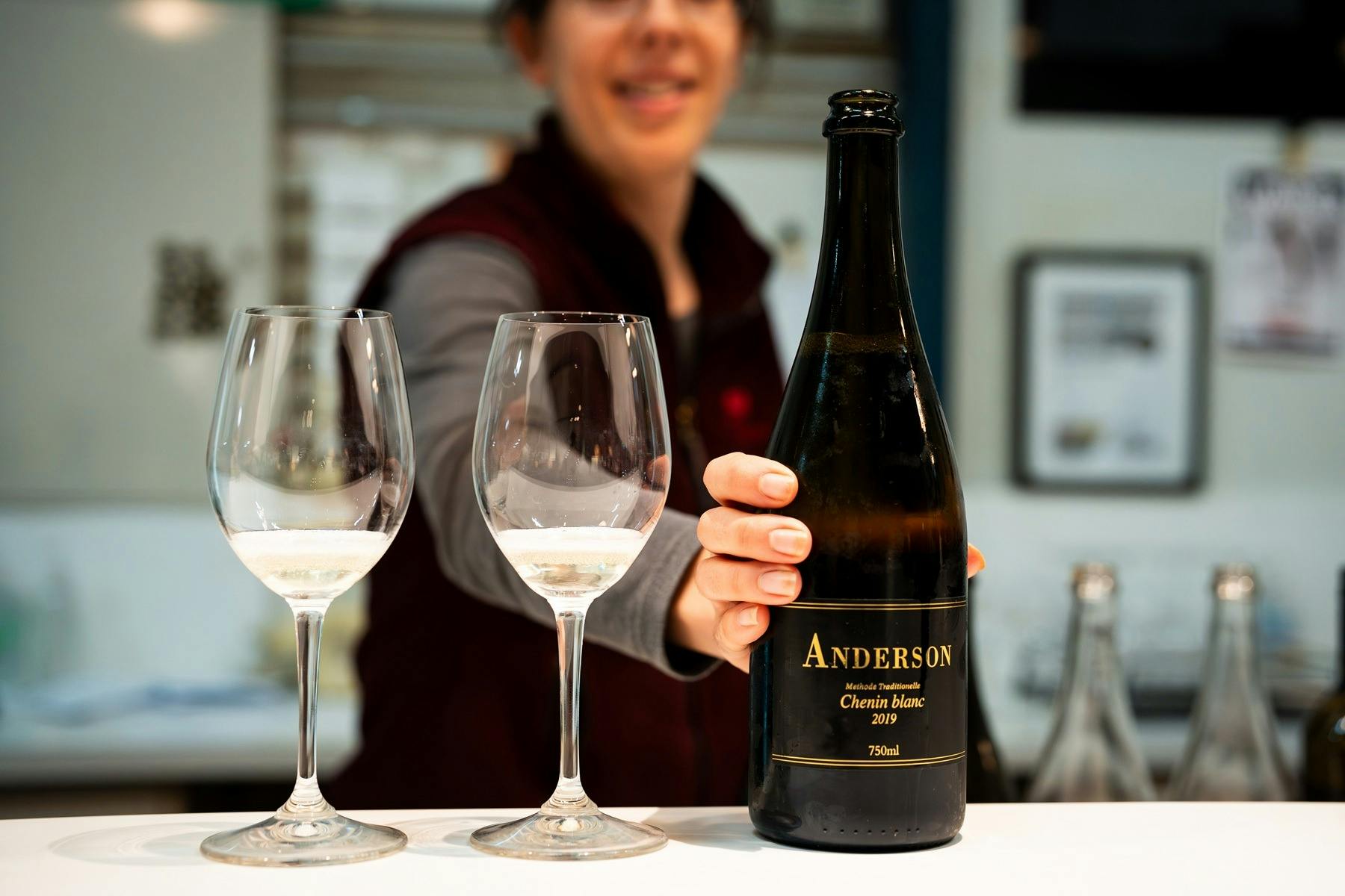 Eine Flasche Anderson Sparkling Chenin Blanc und zwei Gläser werden im Weinkeller serviert.