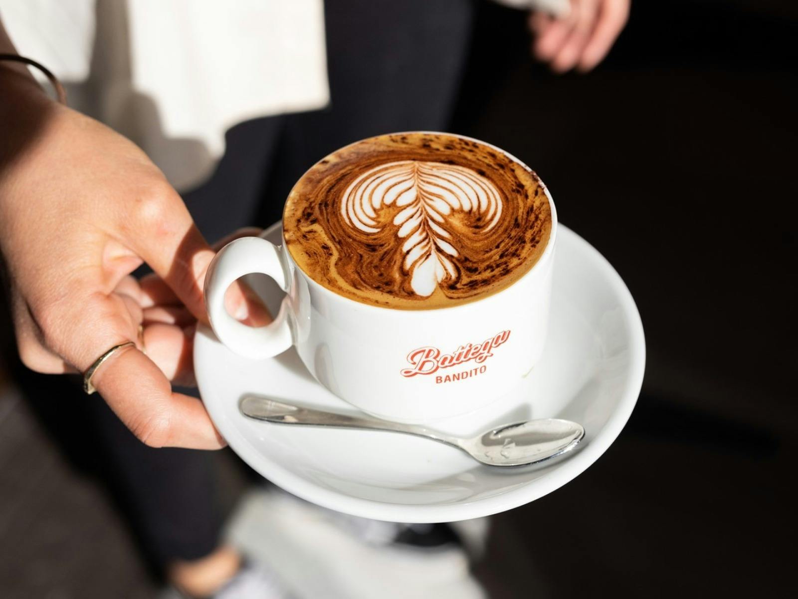 a white mug that saya 'bottega bandito' in red, with froth in the shape of a rosetta