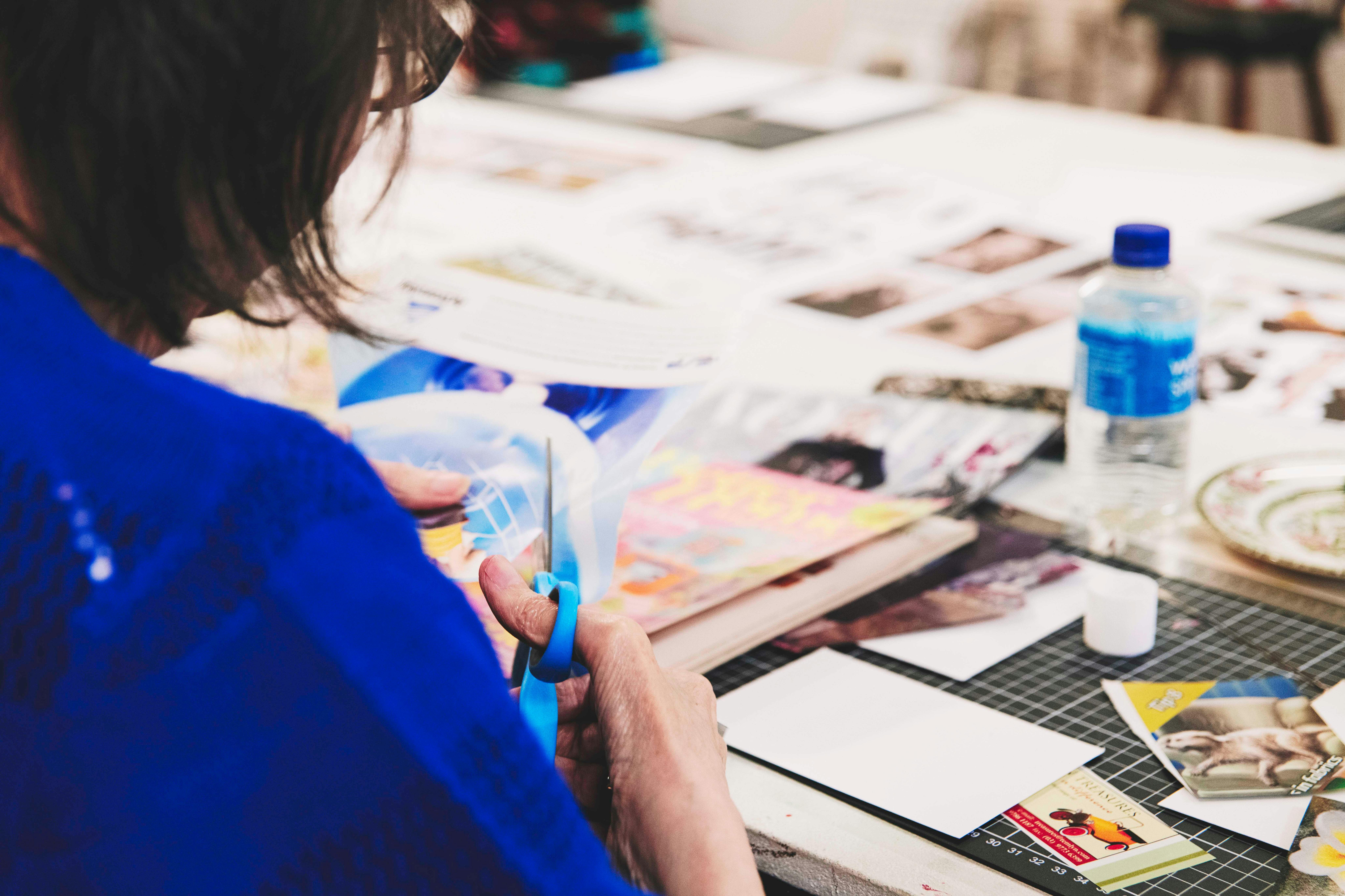 Eine Person schneidet und klebt Elemente aus Zeitschriften und Vintage-Dokumenten auf den Tisch.