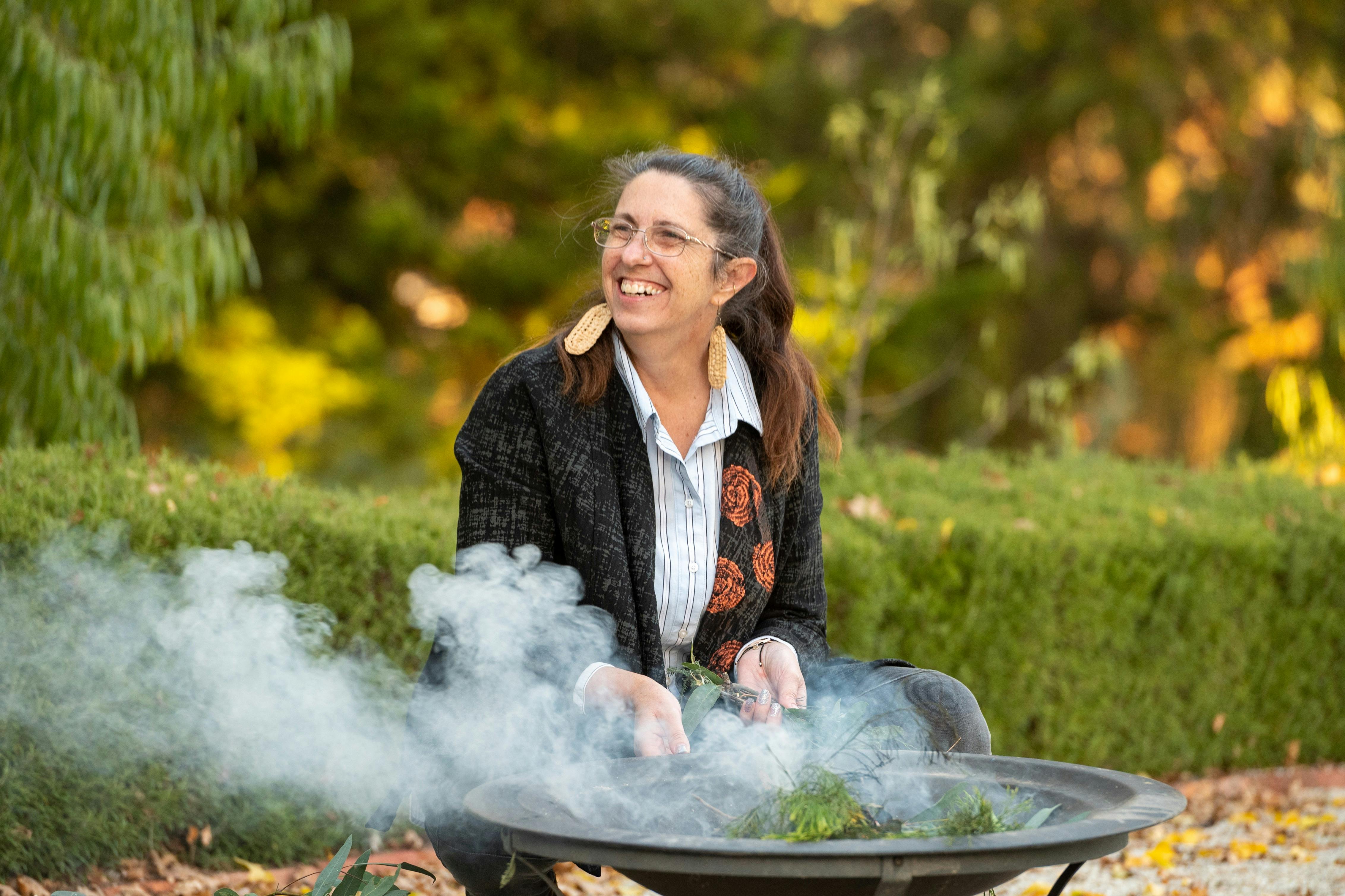 A Djaara woman smiling as she tends a fire a spart of a Smoking Ceremony