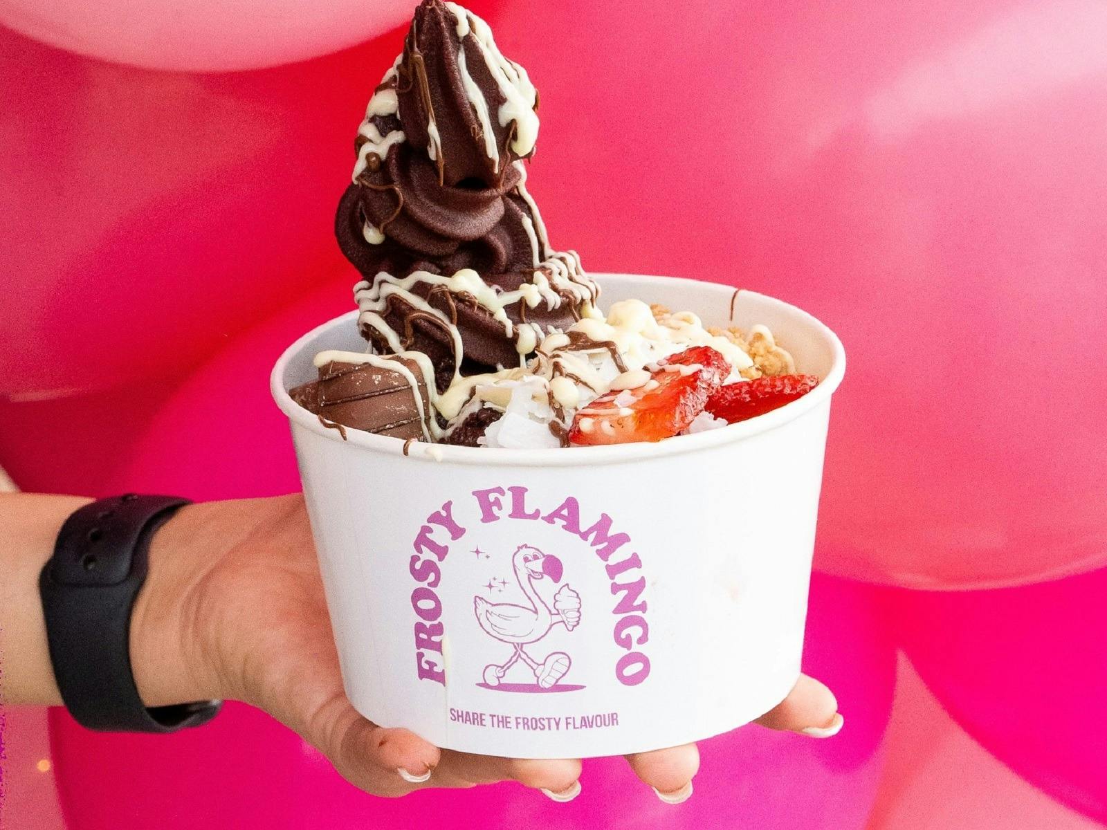 Person holding a ice cream cup of soft serve ice cream with toppings