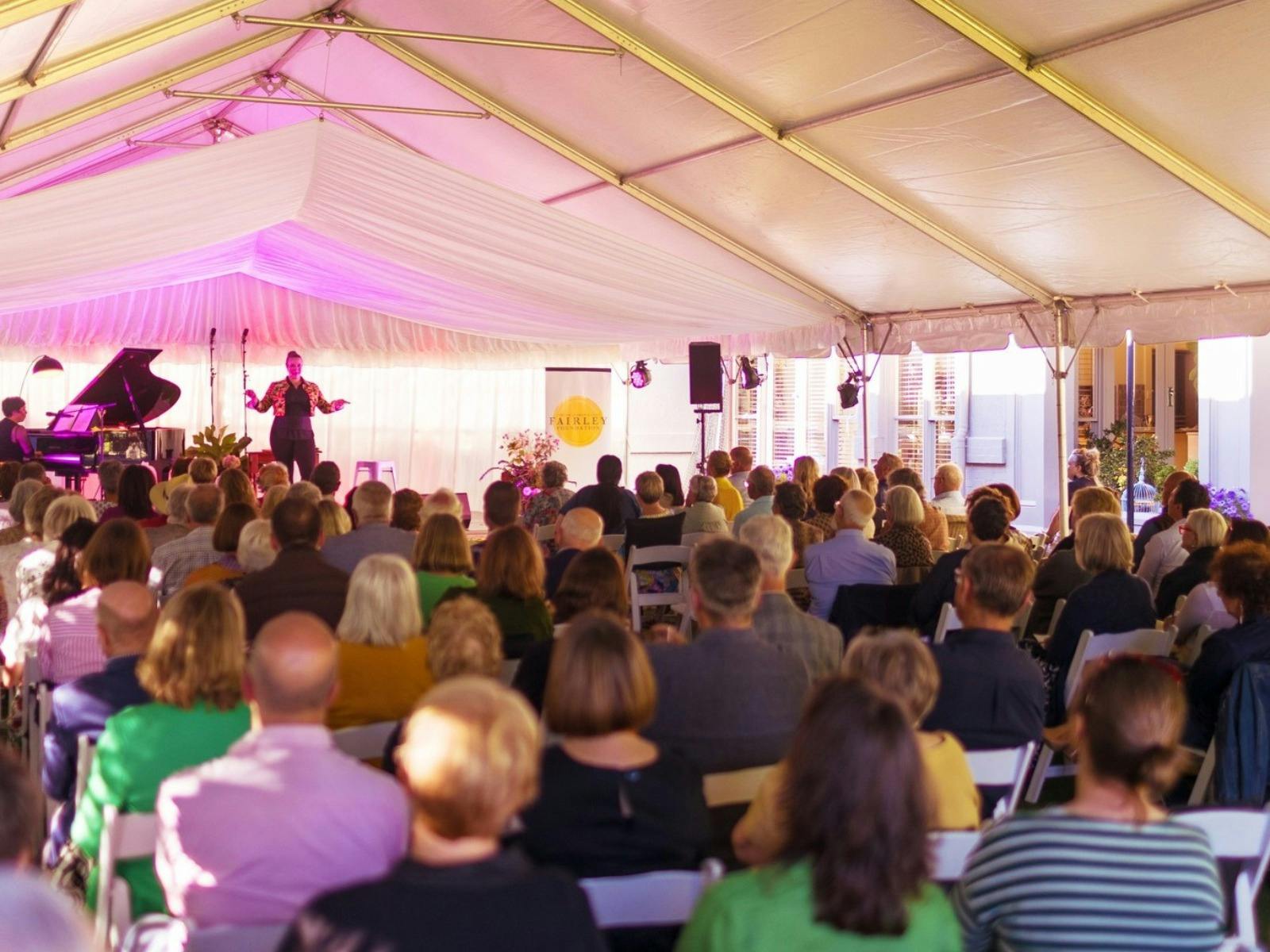 A singer on stage performing with a pianist while a large crowd watches on