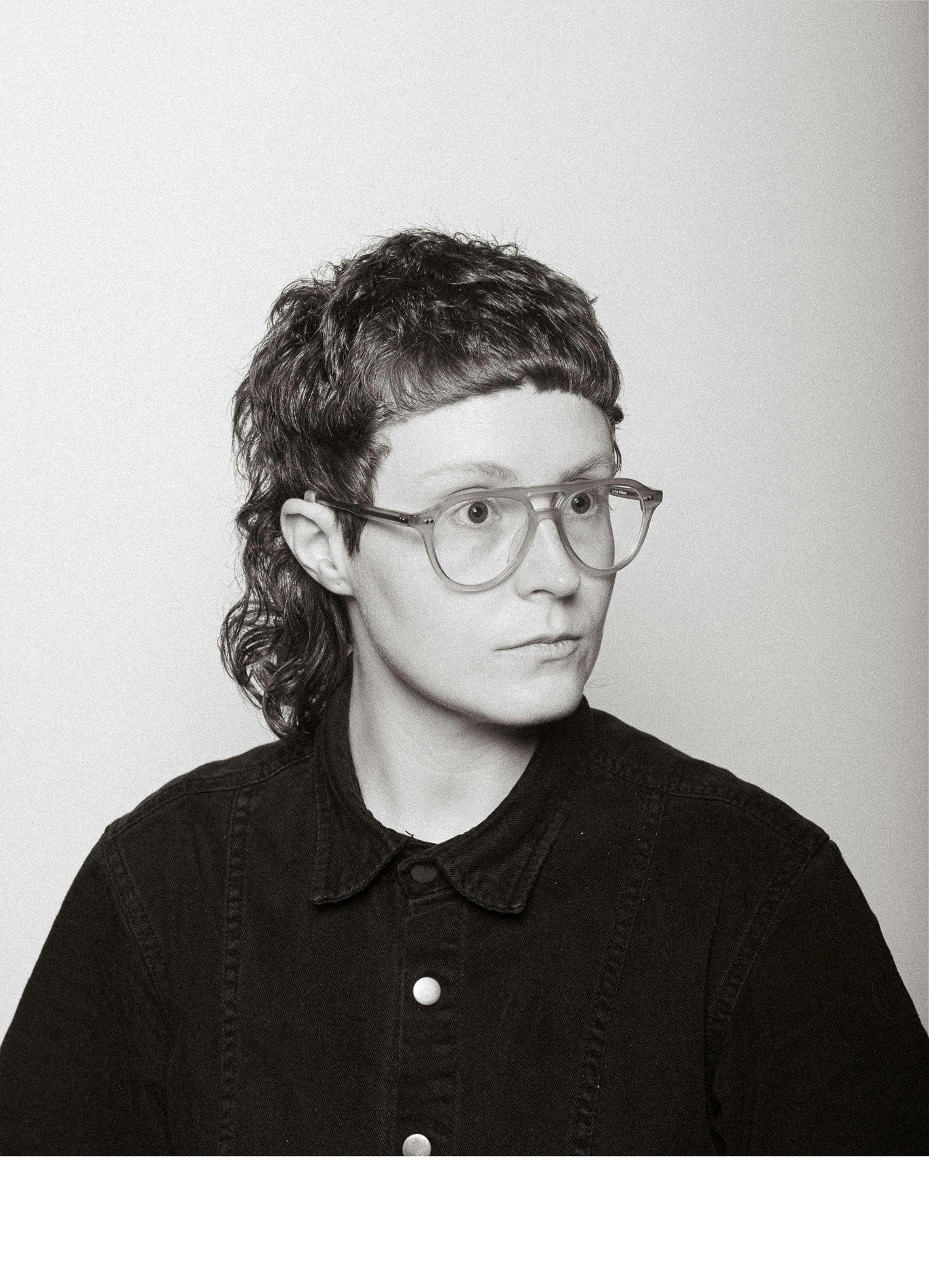 A black-and-white photo of a person with short curls and glasses.