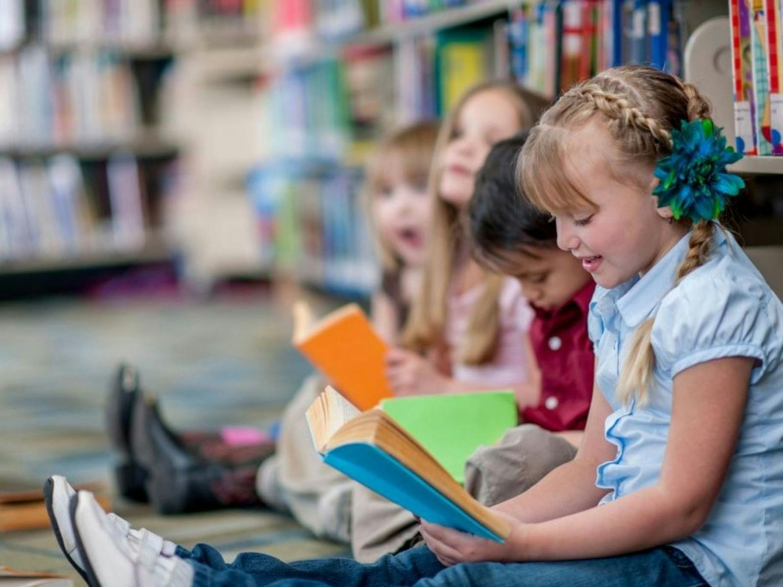 kids leaning against bookshelves reading books