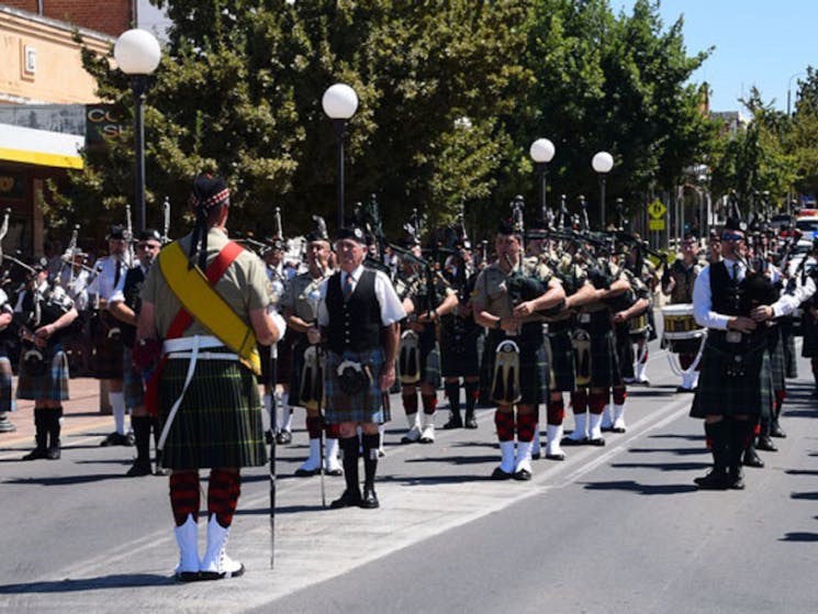 Group of Soldiers dressed in Kilts carrying Pipes and Drums and marching down the street.