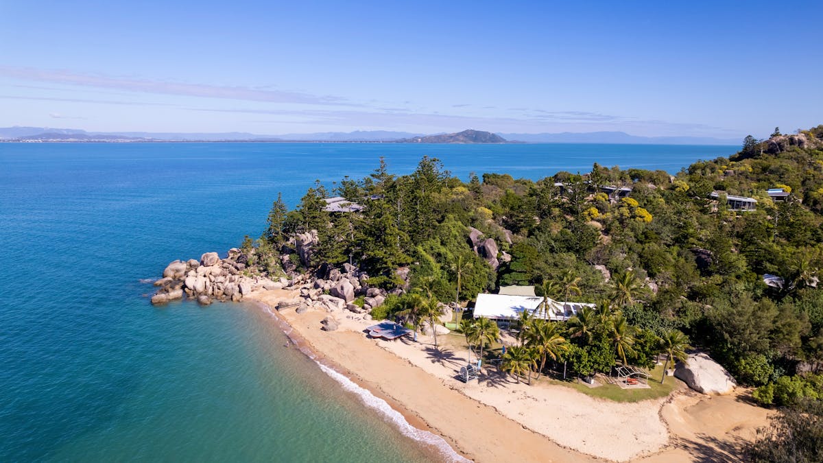 Drone shot of Picnic Bay beach with houses hidden in the trees and amongst the hills