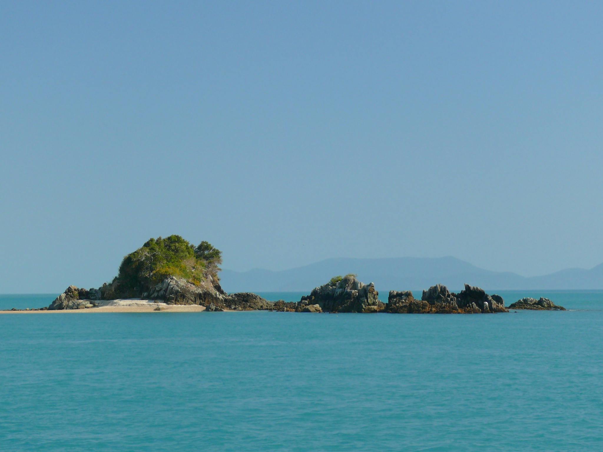 Full view of the small and rocky Henning island with a stretch of sand on the left side Full view of the small and rocky Henning island with a stretch of sand on the left side
