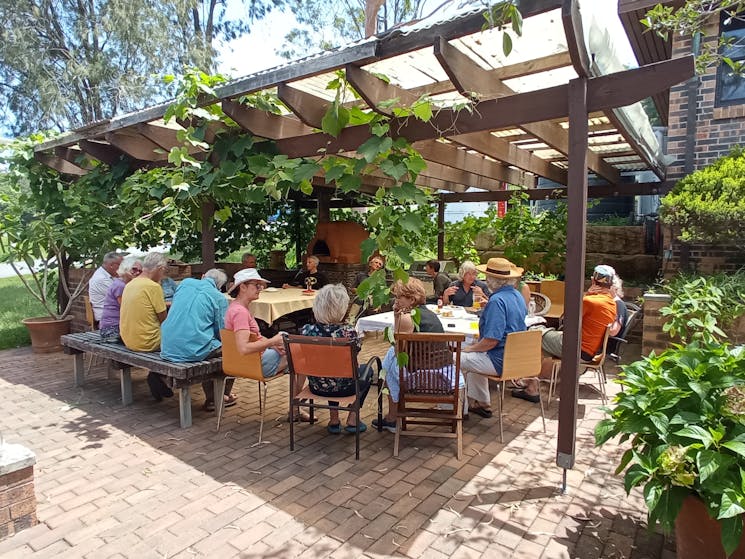 20 members sit under the shade of the awning in the Members' Courtyard  for a summer lunch
