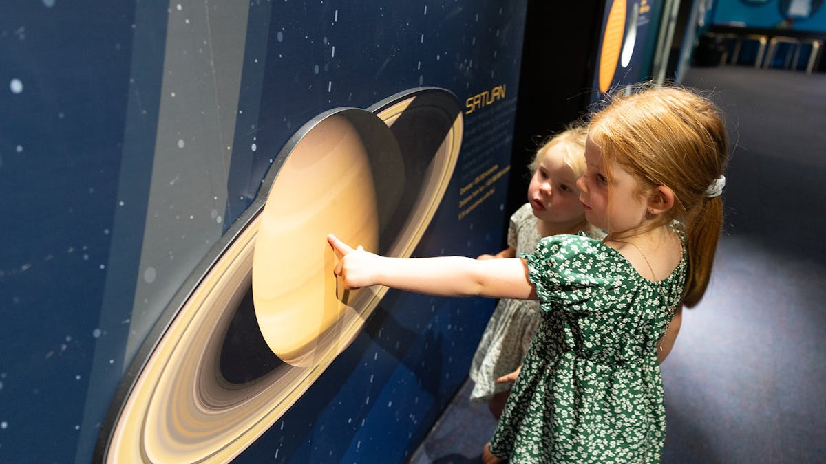 Kids in our Solar System area, pointing at Saturn.