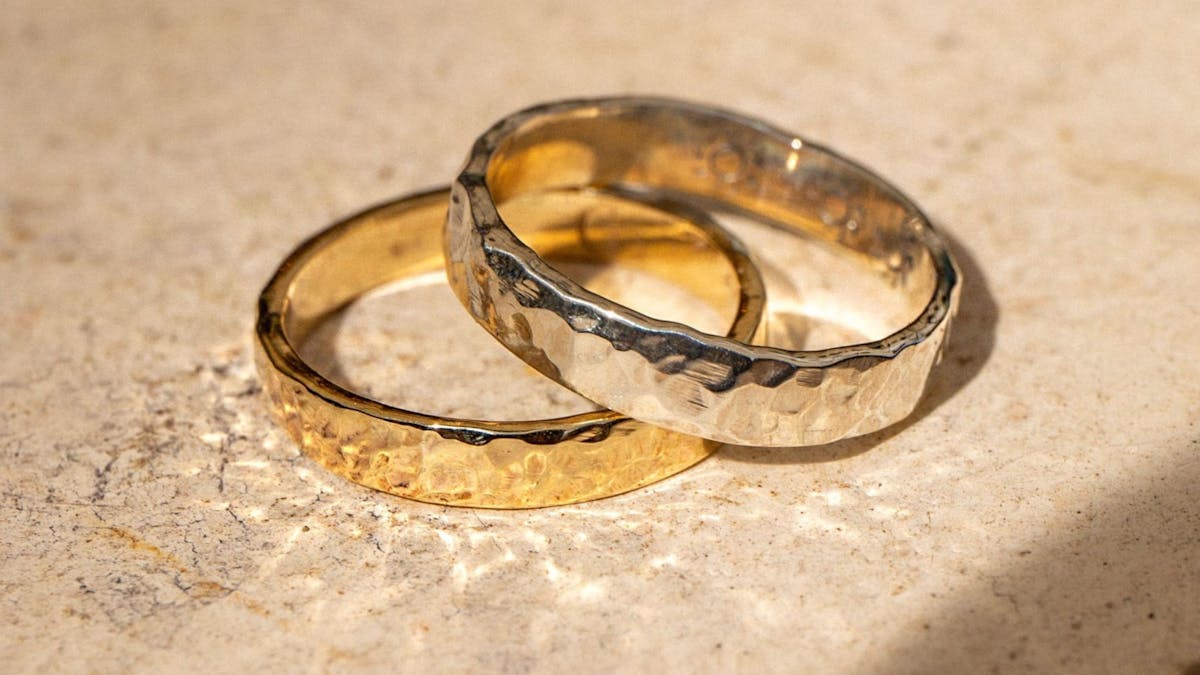 Two handcrafted hammered rings, one gold and one silver, placed on a textured stone surface.