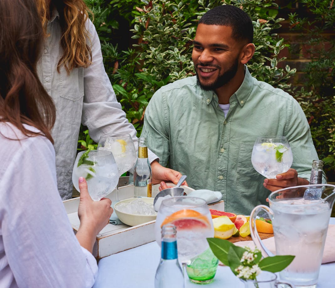 Group of people sitting outdoors, smiling and holding large gin and tonic glasses