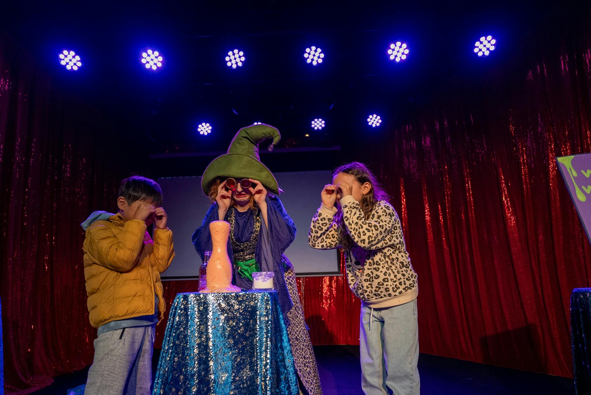 Wizard and 2 children on stage with their safety shmoggles while potion overflows