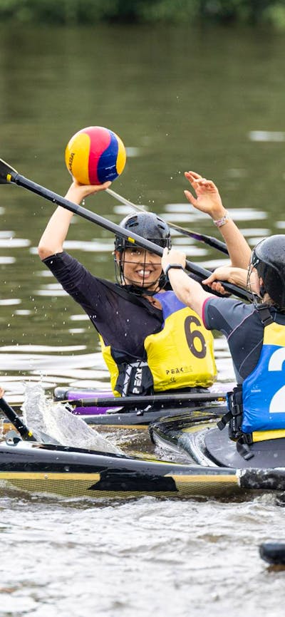 Four players are on the field. One woman (yellow team) is ready to throw the ball