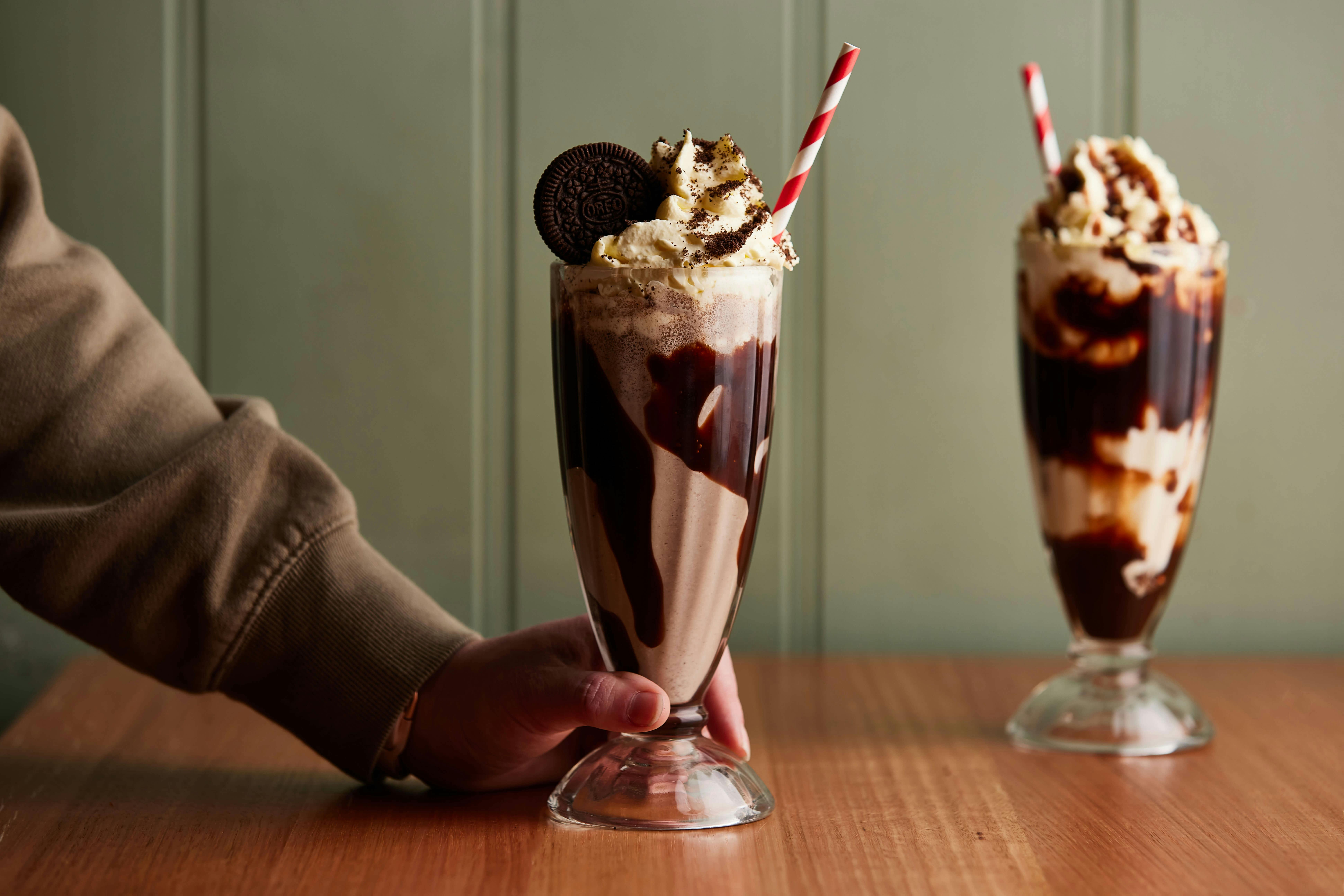 Two milkshakes with red and white striped paper straws sit in the foresground