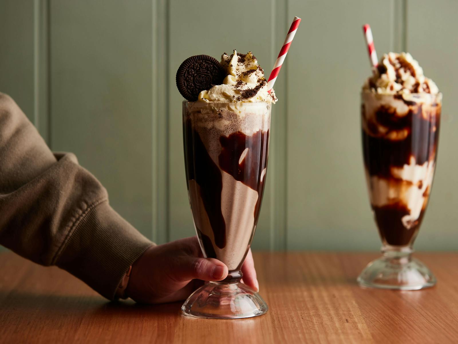 Two milkshakes with red and white striped paper straws sit in the foresground