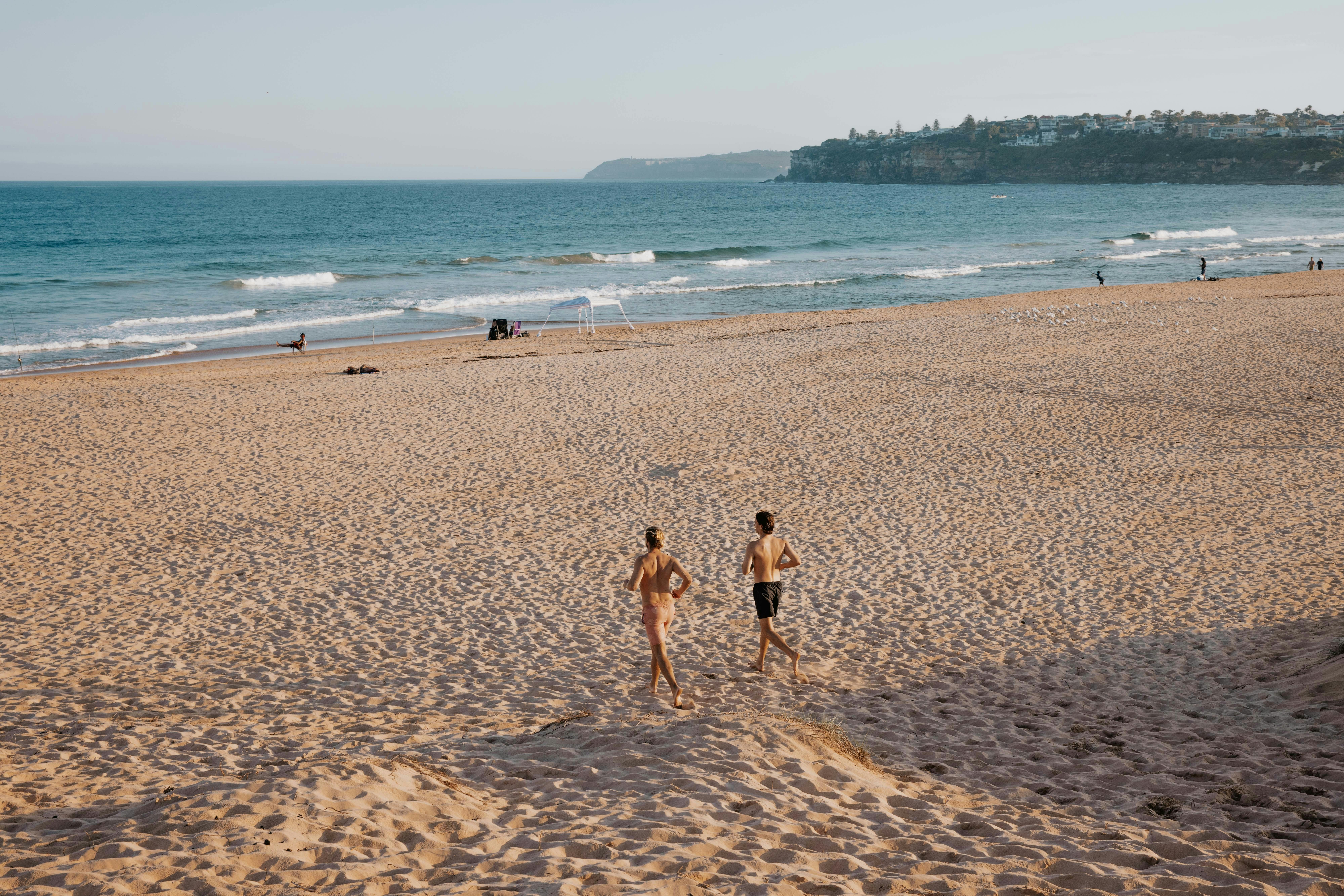 2 guys running to the beach after having a mobile outdoor woodfire sauna