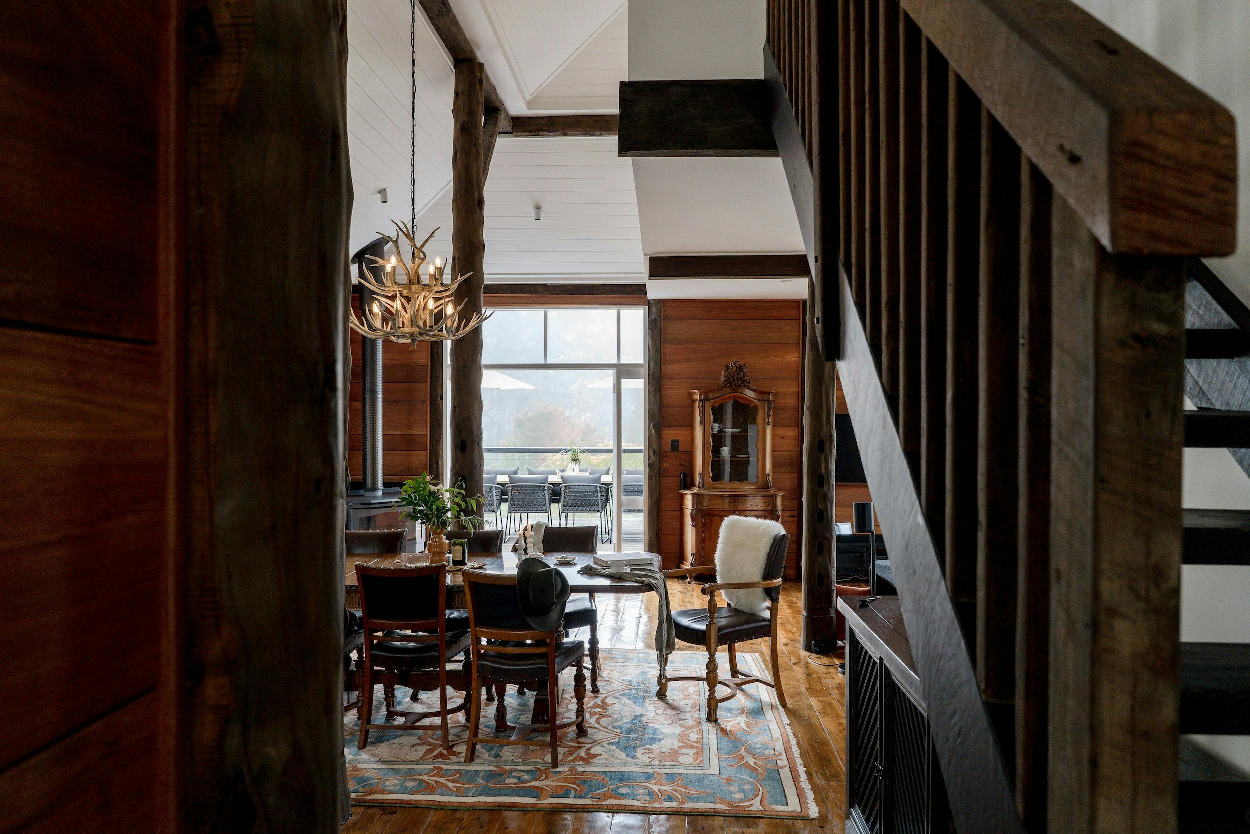 An image of a dining room with timber table, antler chandelier and vintage rug