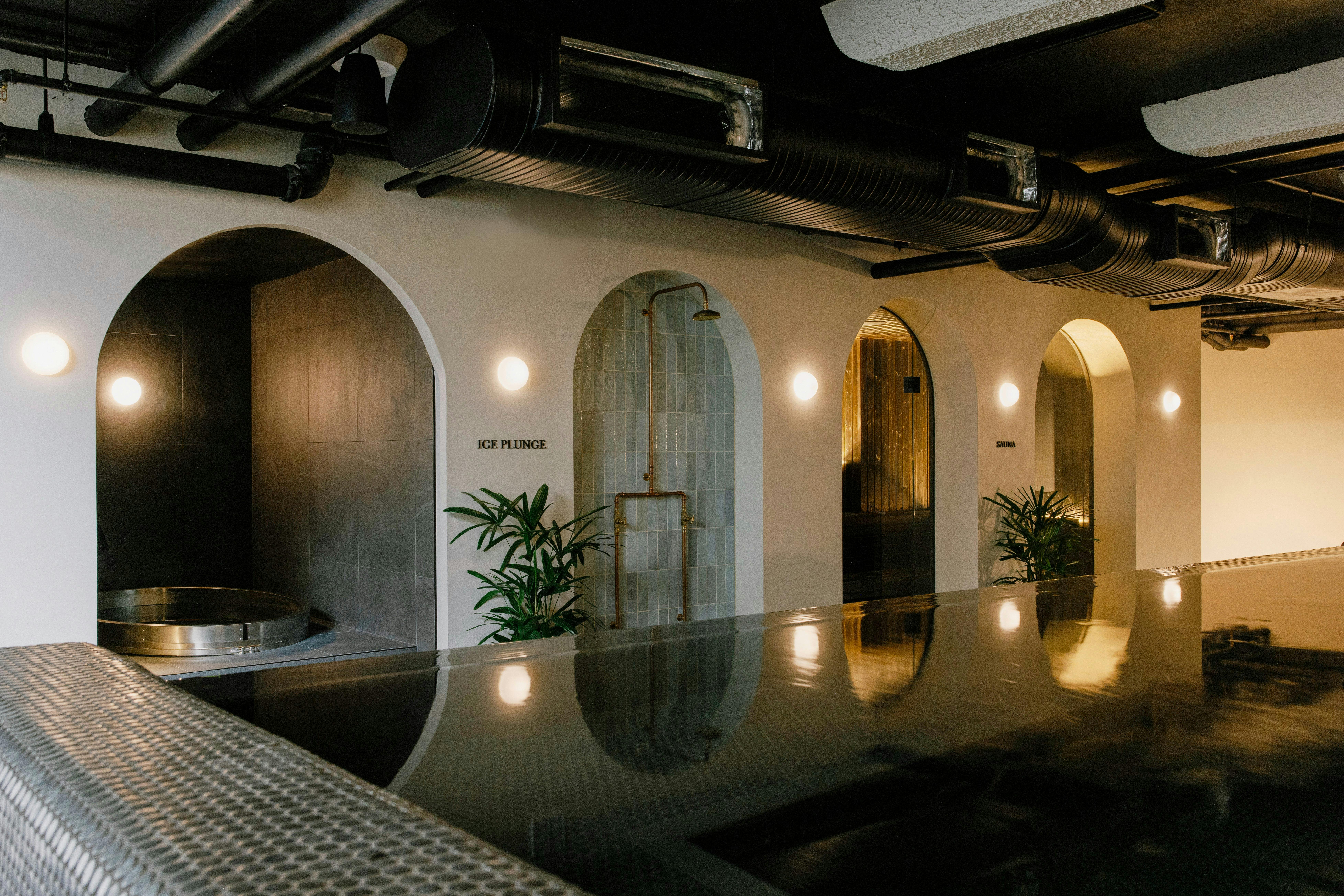 The black tile mineral hot pool in the foreground, with Navia's arched entrances to the sauna & pool