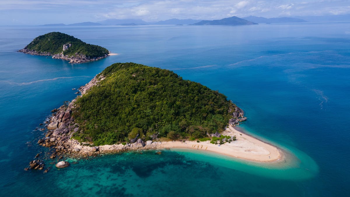 A  tiny, pristine tropical island sits in crystal aqua waters with islands dotting into the distance