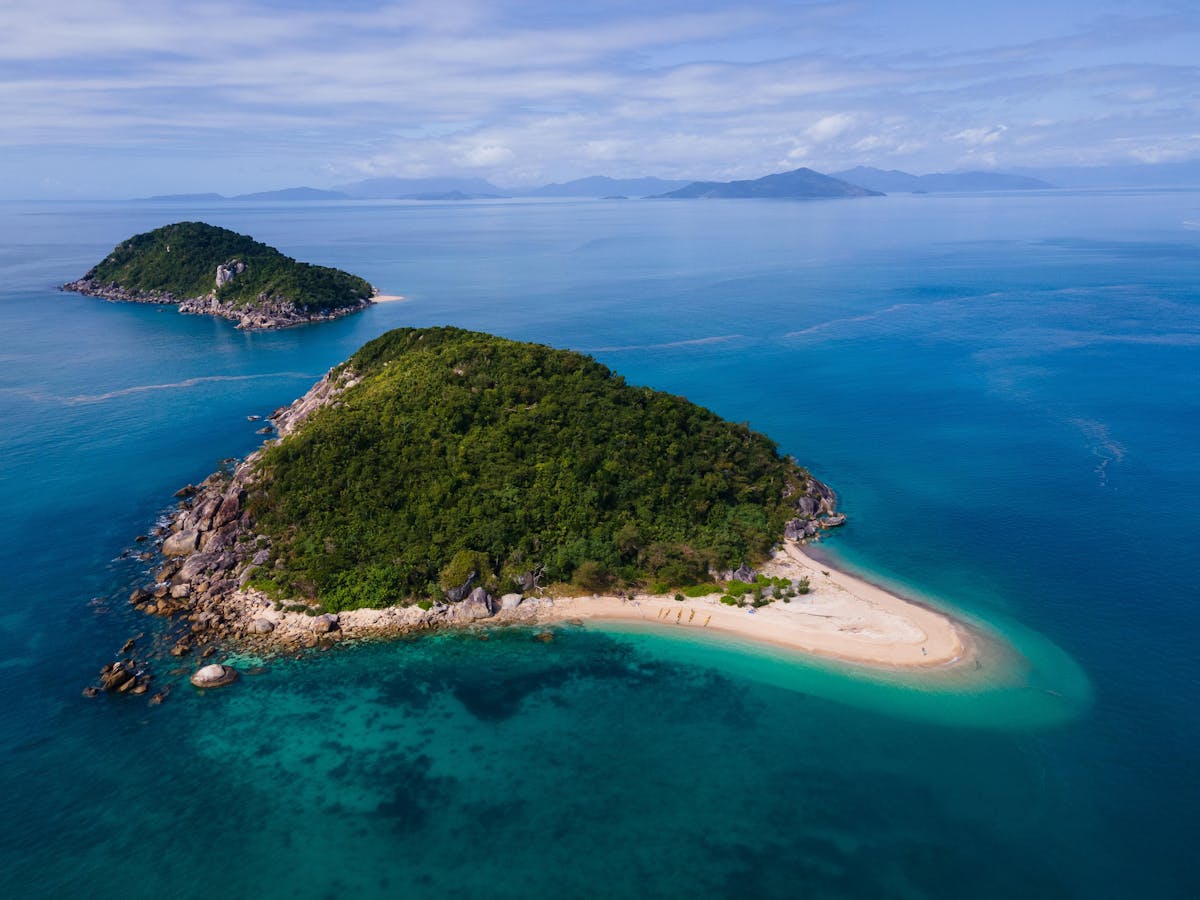 A tiny, pristine tropical island sits in crystal aqua waters with islands dotting into the distance