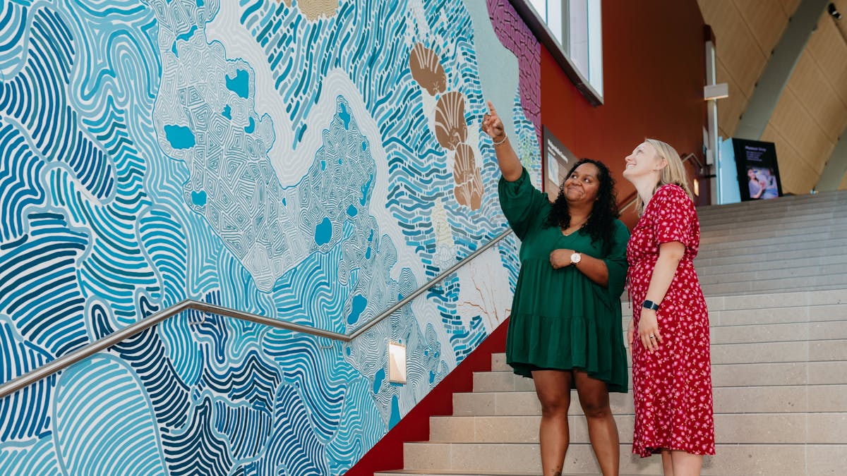 2 women looking at an indigenous mural