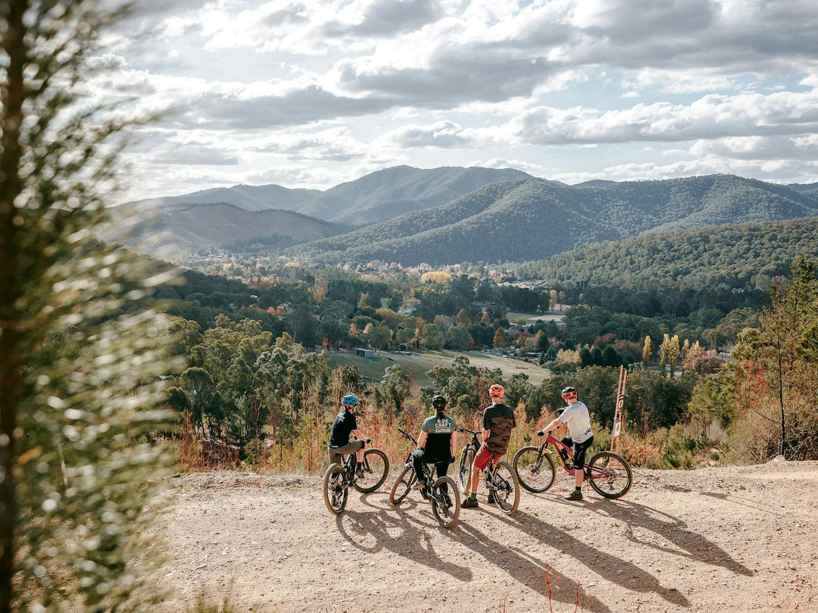 Four riders stand with their backs to the camera overlooking a valley with mountain views