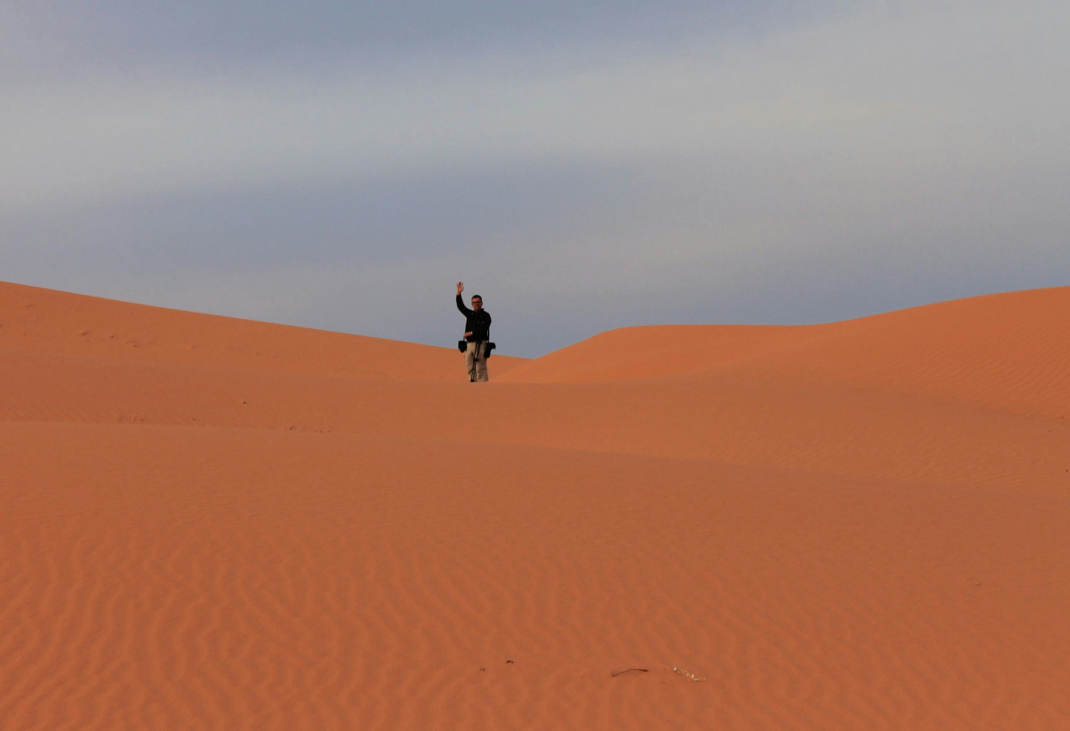 man standing in the middle of a big red sand dune