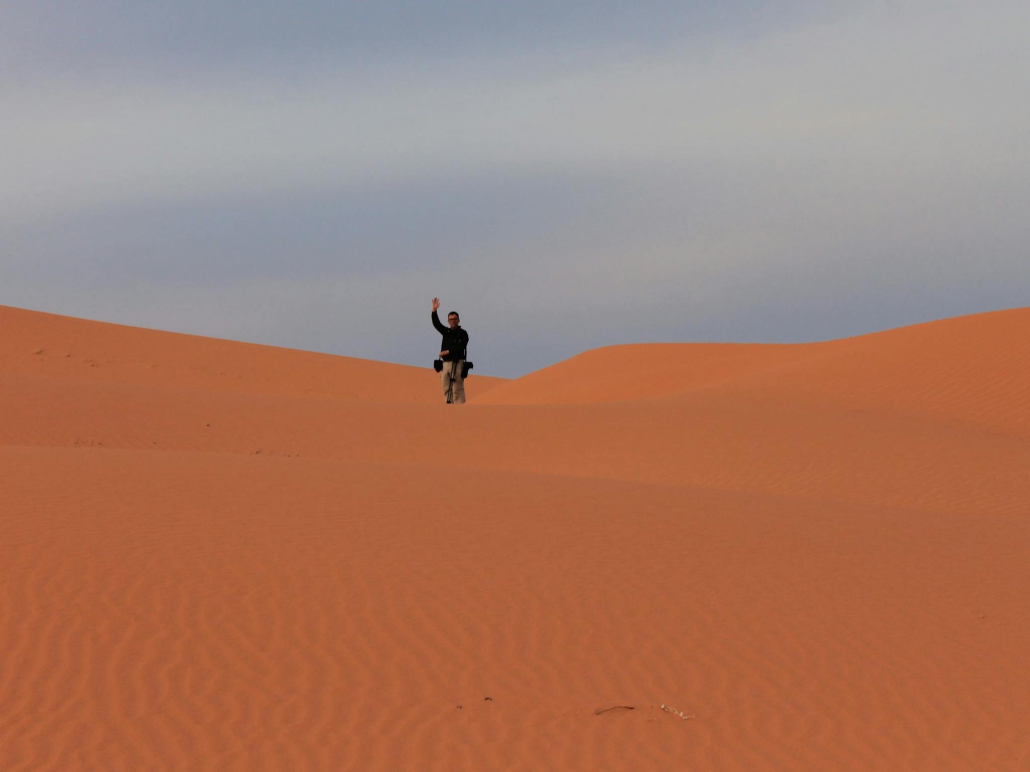 man standing in the middle of a big red sand dune
