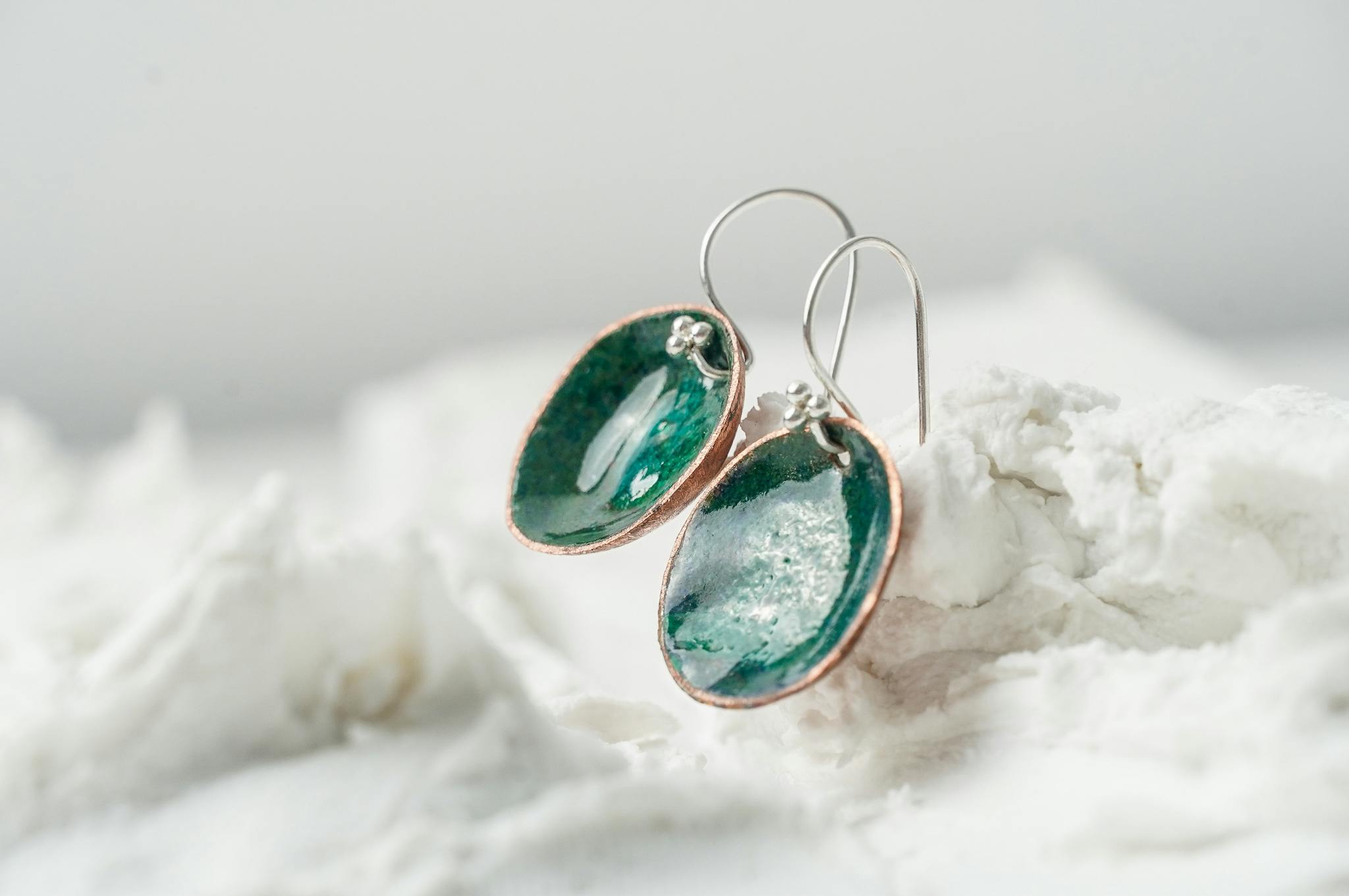 A pair of deep green enamelled copper earrings on a white background.